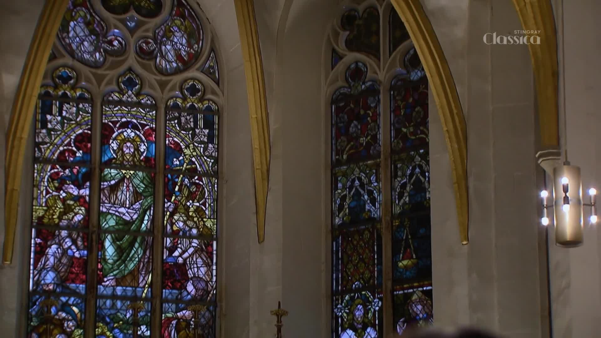 Sunlight streams through the intricate stained-glass windows of this Canadian church, illuminating scenes from scripture. A modern light fixture hangs to the right, casting a warm glow.