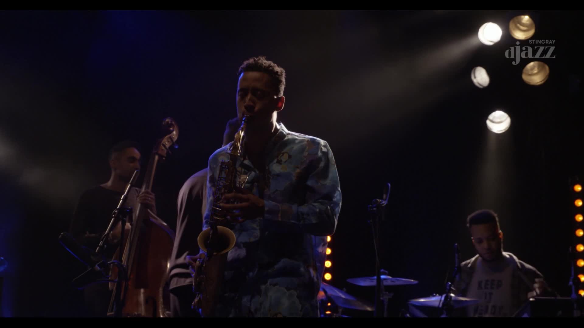 A saxophonist, in a patterned shirt, holds the stage's focus as he plays. The band, illuminated by stage lights, provides the rhythm and sound for this Canadian performance on Stingray DJAZZ.
