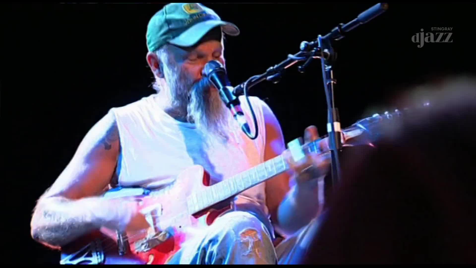 The guitarist, sporting a green cap, strums a red electric guitar, his fingers a flurry on the fretboard. He leans into the microphone, singing under the lights of a performance on Stingray DJAZZ.
