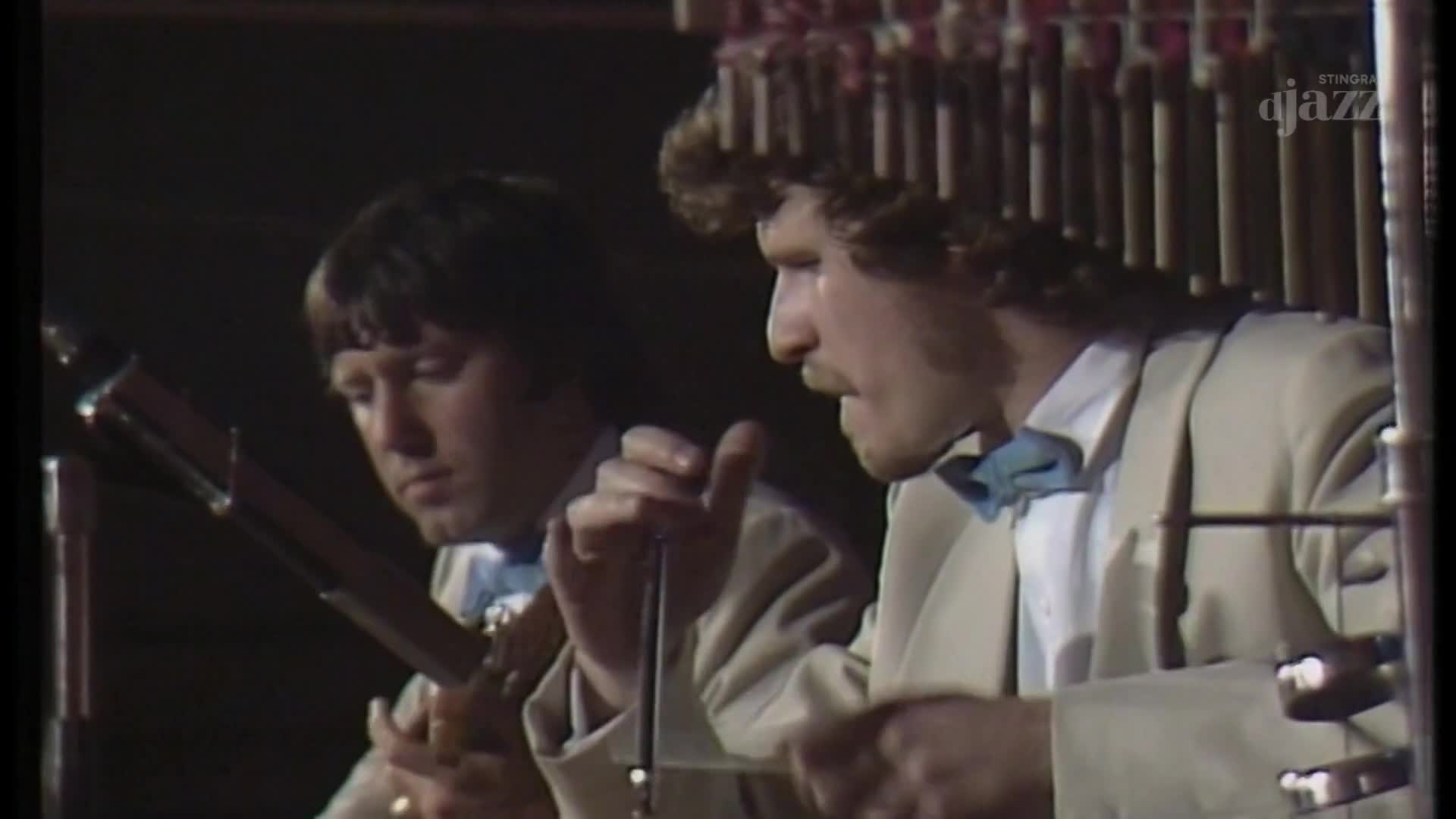 Two men in matching jackets and bow ties are focused on their instruments, one playing a stringed instrument and the other manipulating a theremin. The Stingray DJAZZ logo is visible, indicating this is a broadcast from Canada.
