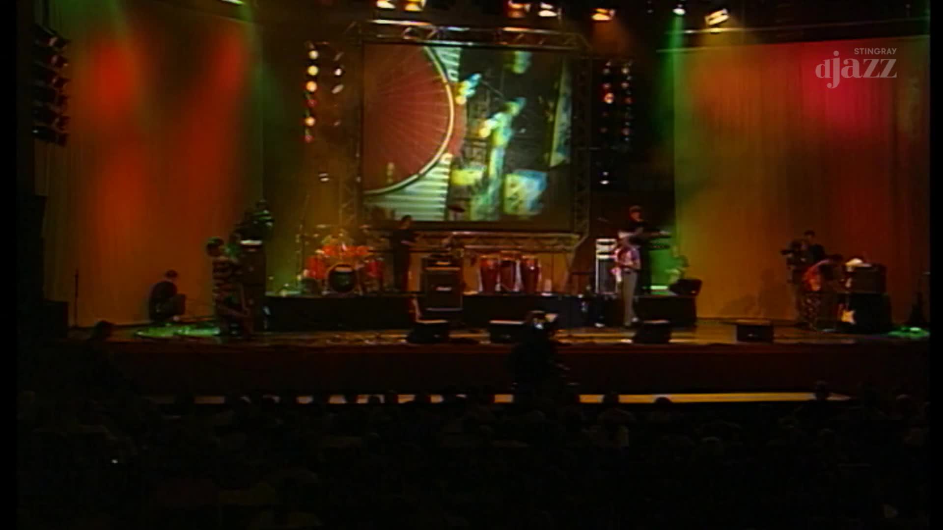 On a stage lit with red and green, a band performs, their images projected on a screen behind them. The Stingray DJAZZ logo is visible as the music fills the Canadian venue.
