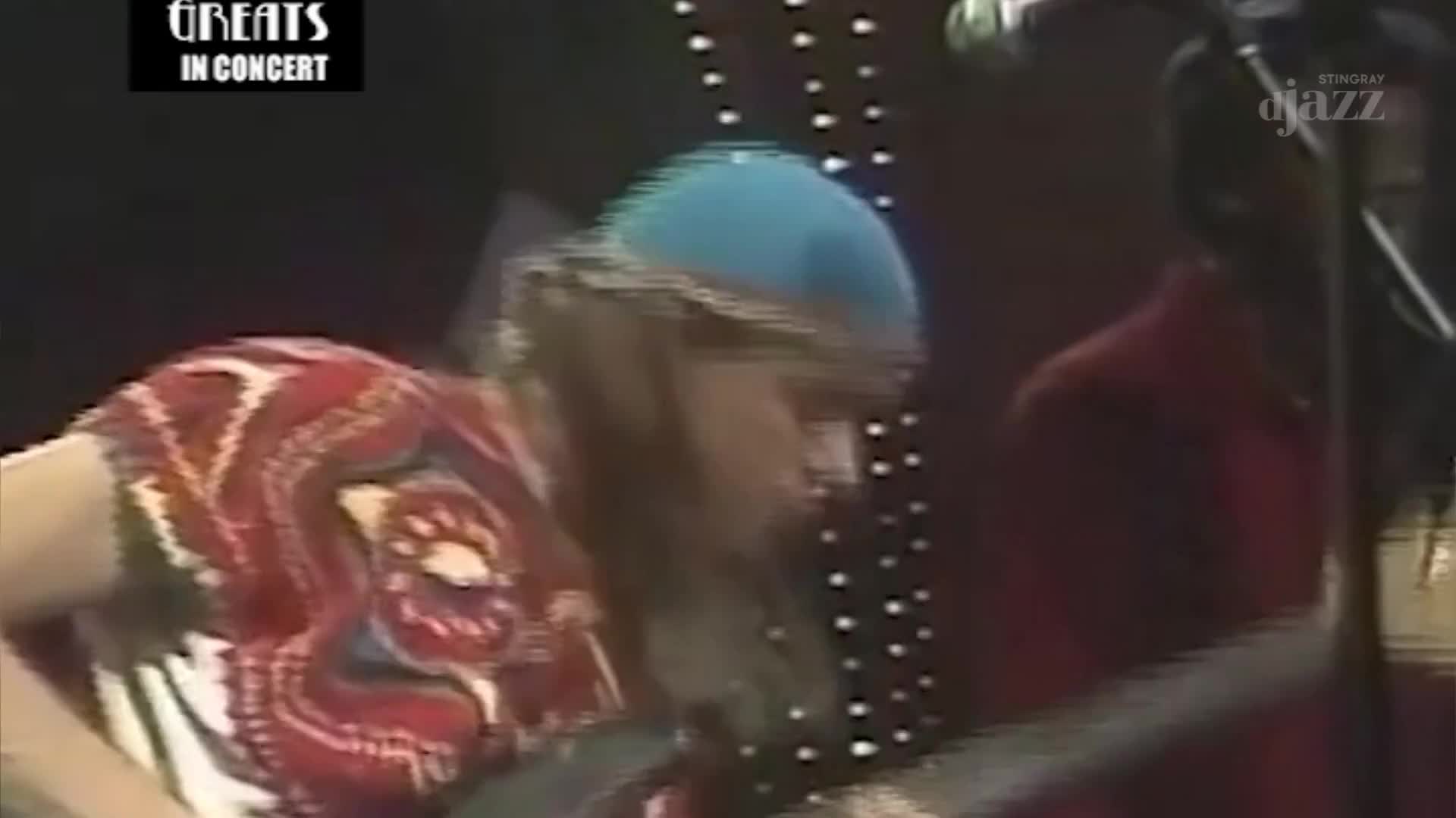 A musician in a patterned shirt and blue cap is focused on their instrument, likely a bass guitar. The Stingray DJAZZ logo is visible, suggesting a Canadian concert recording.

