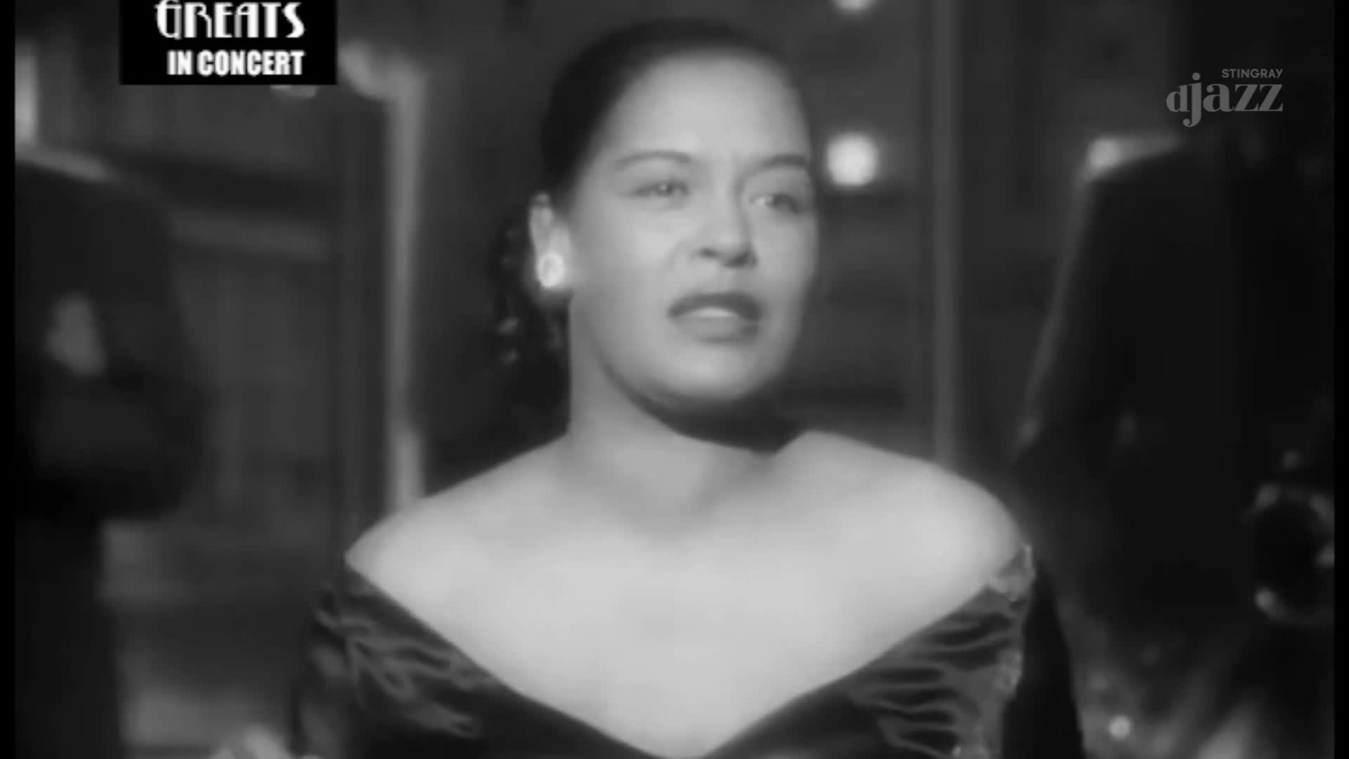 The singer, lit by a single spotlight, looks directly at the camera, her mouth open as if she's about to sing. The Stingray DJAZZ logo is visible on the right, and the "Greats in Concert" banner floats above.
