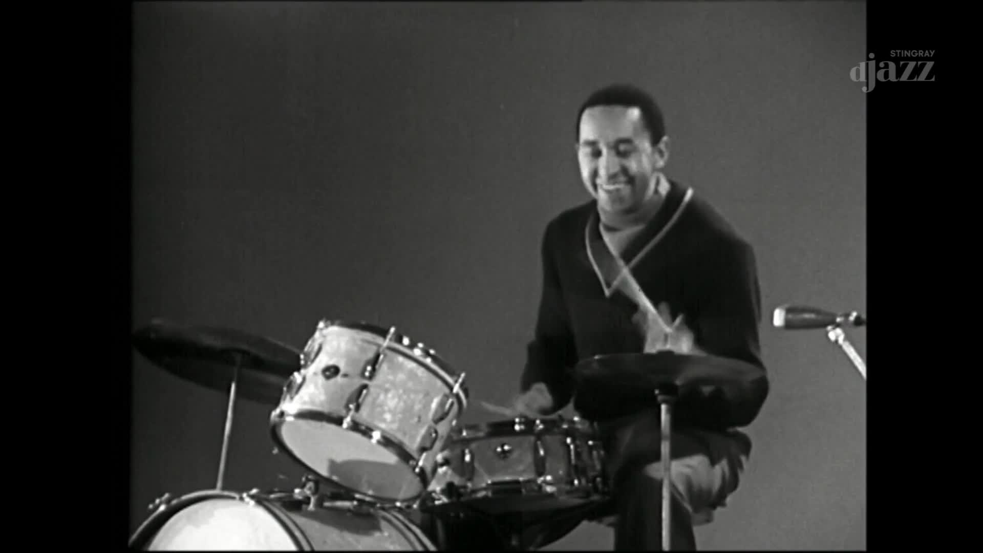 A drummer, smiling, is hitting the cymbals and snare with a steady rhythm. The camera is focused on the man and his kit, broadcasting from Canada on Stingray DJAZZ.
