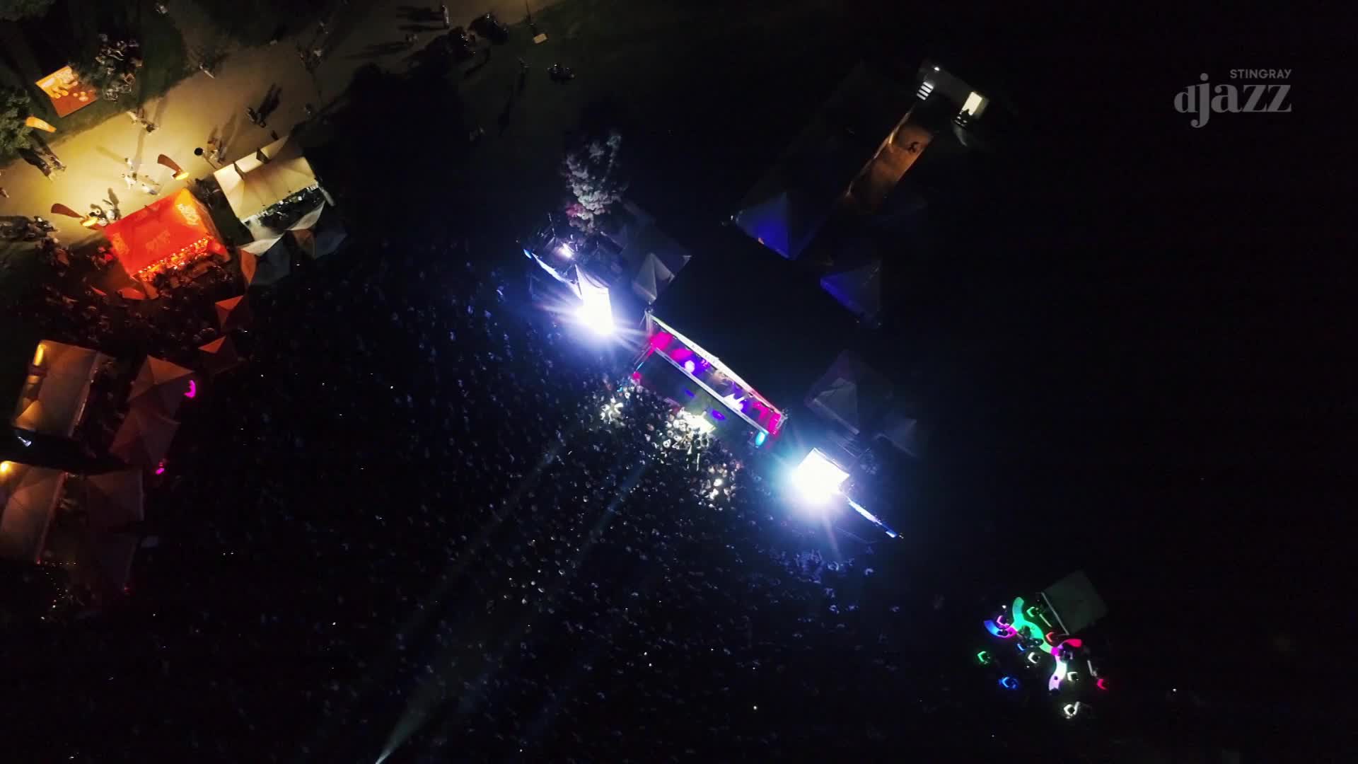 Under the night sky, a large crowd gathers, bathed in the bright stage lights. The Stingray DJAZZ logo sits in the corner, and the scene is alive with music and energy.
