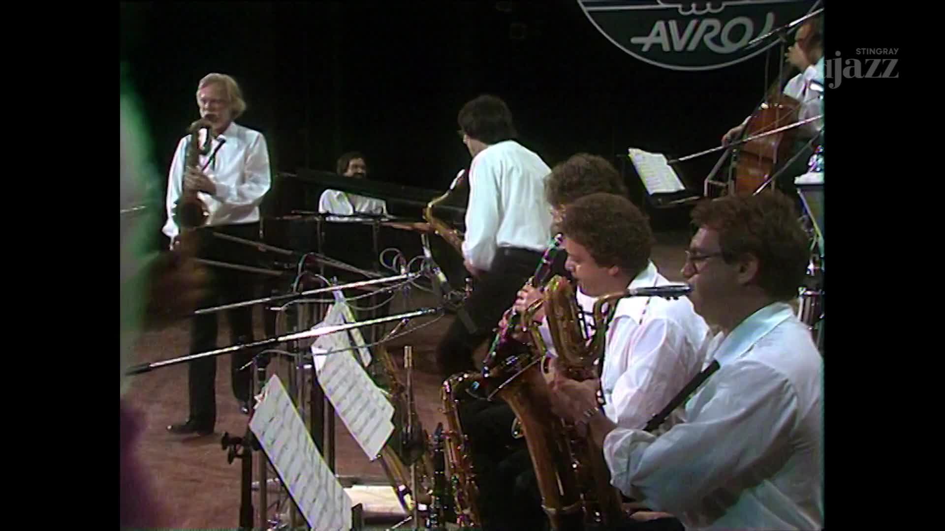 A jazz ensemble, likely from Canada, is performing on stage, with a Stingray DJAZZ logo visible. The saxophonists are intently focused, their instruments raised, while a cellist and keyboardist add to the music.
