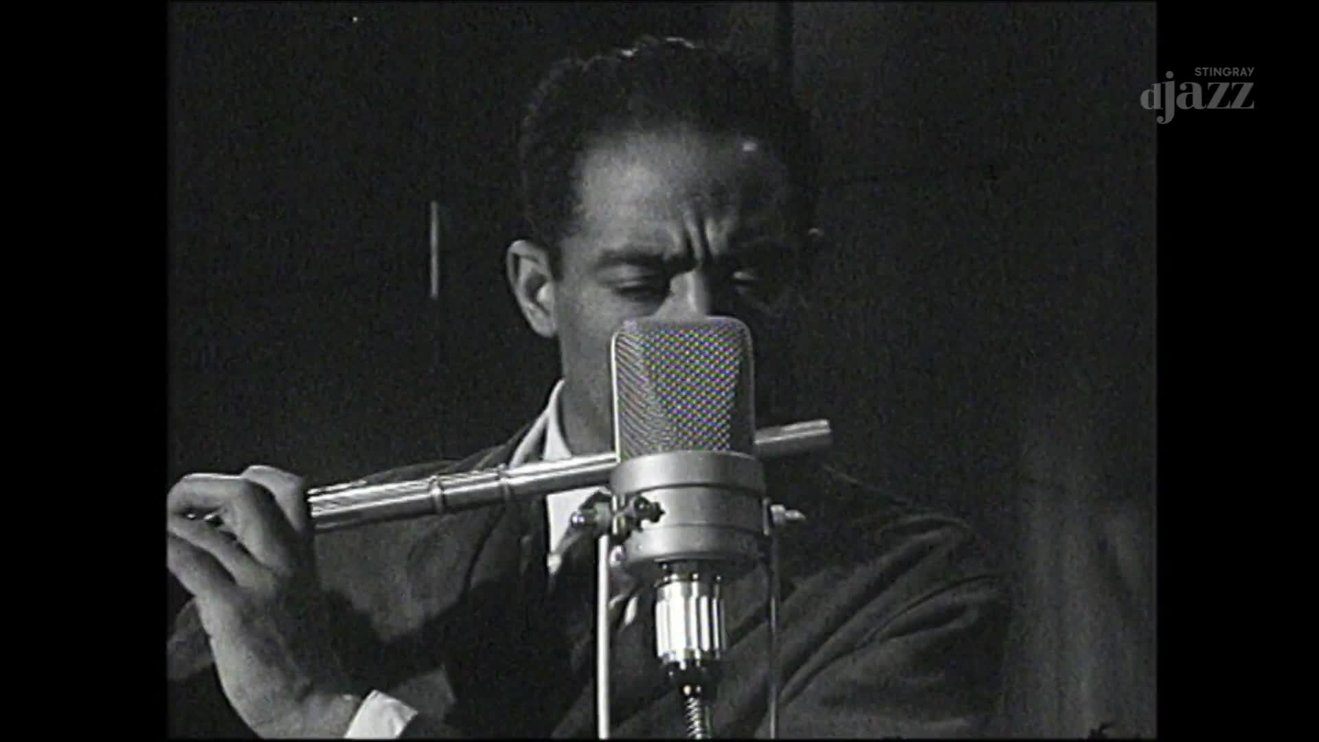 A musician, framed by a vintage microphone, holds a flute to his lips. The Stingray DJAZZ logo appears in the corner of the screen, suggesting this is a broadcast from Canada.
