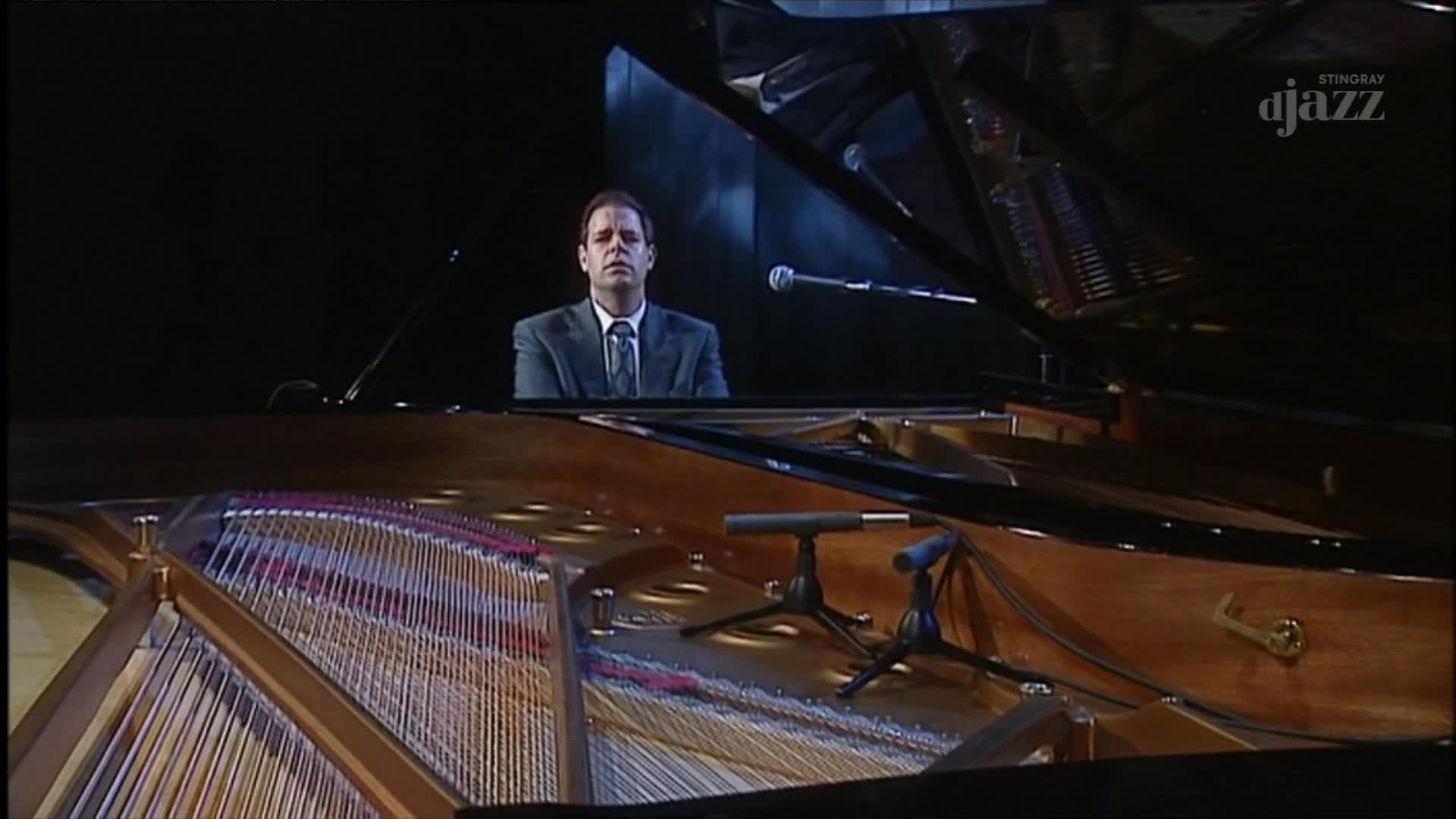A man in a suit sits at a grand piano, the strings and soundboard visible. The Stingray DJAZZ logo suggests we're in Canada, watching a performance.
