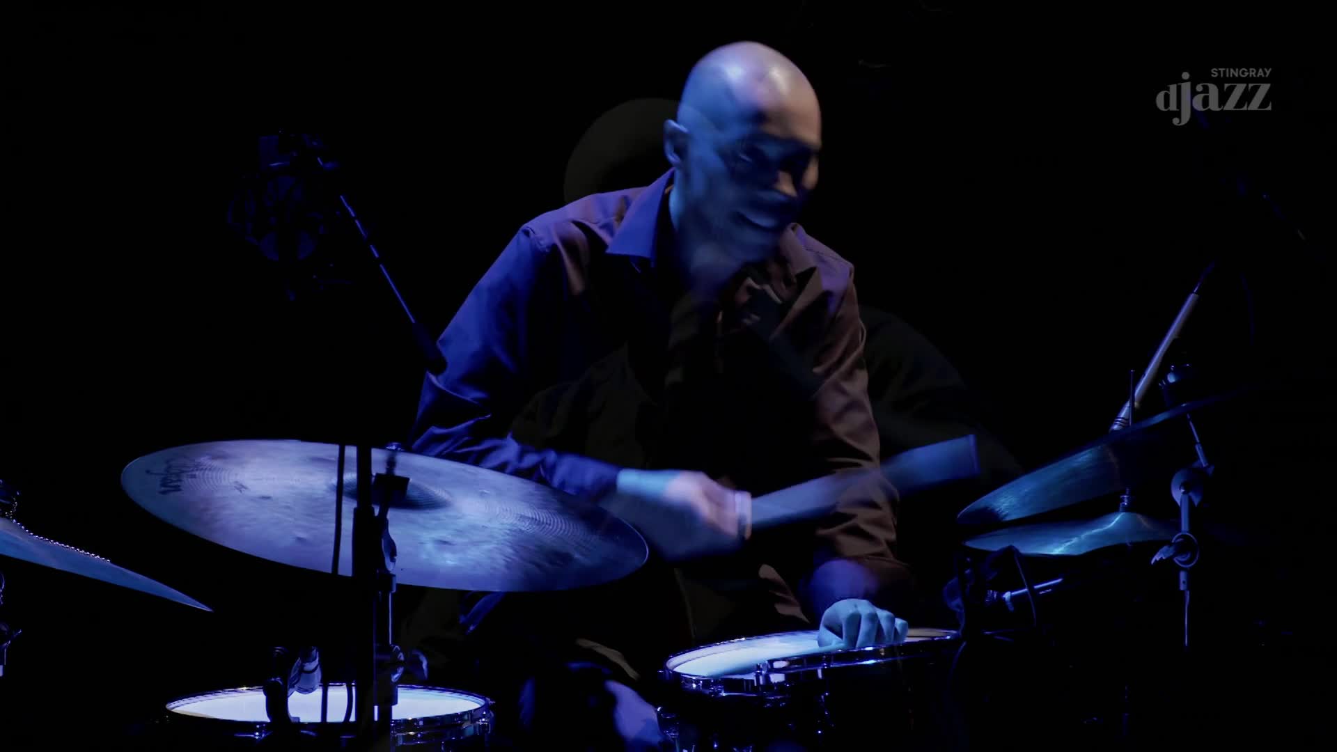 A drummer, lit by blue light, is mid-beat, his sticks a blur as they strike the cymbals. The Stingray DJAZZ logo is visible in the corner, and the whole scene has a cool, Canadian vibe.
A drummer, lit by blue light, is mid-beat, his sticks a blur as they strike the cymbals. The Stingray DJAZZ logo is visible in the corner, and the whole scene has a cool, Canadian vibe.