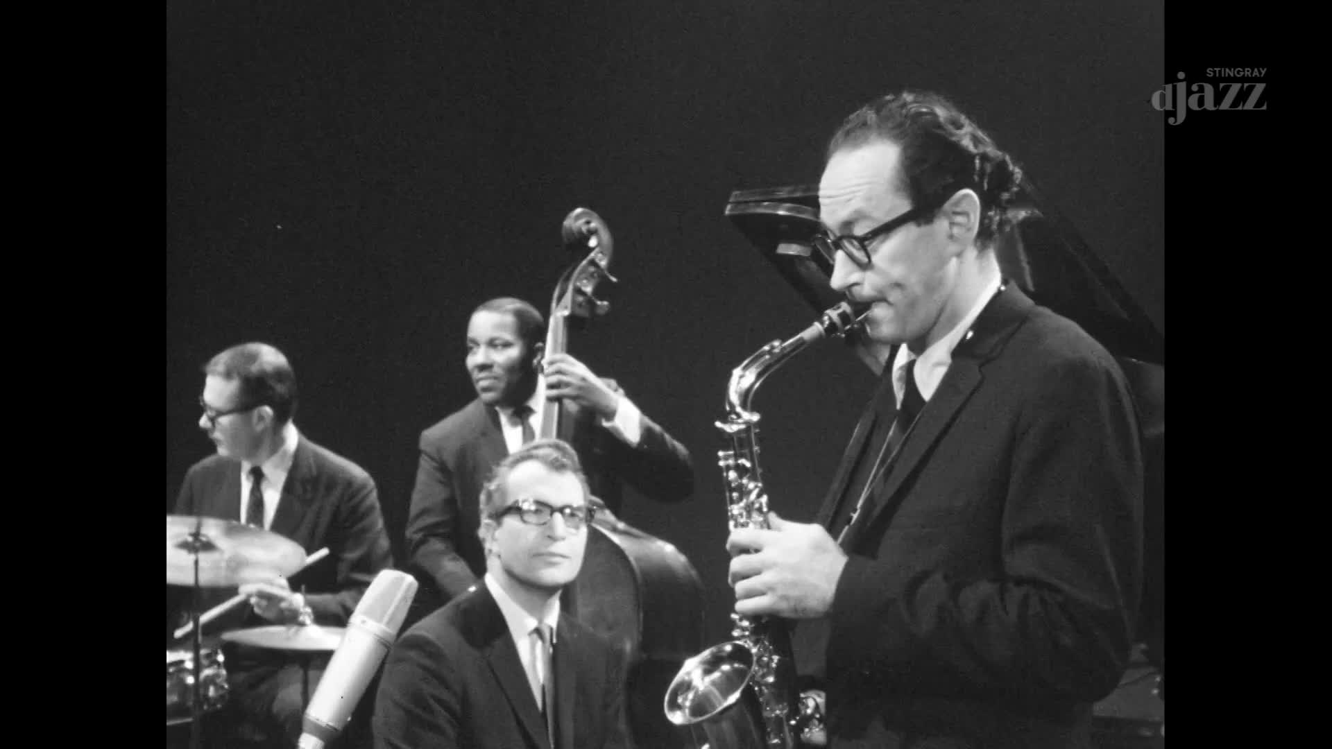 The saxophonist, in a dark suit and glasses, blows into his instrument, his cheeks puffed out. A bassist and drummer provide the rhythm, while a pianist sits behind them, all set for a jazz session.
The saxophonist, in a dark suit and glasses, blows into his instrument, his cheeks puffed out. A bassist and drummer provide the rhythm, while a pianist sits behind them, all set for a jazz session.