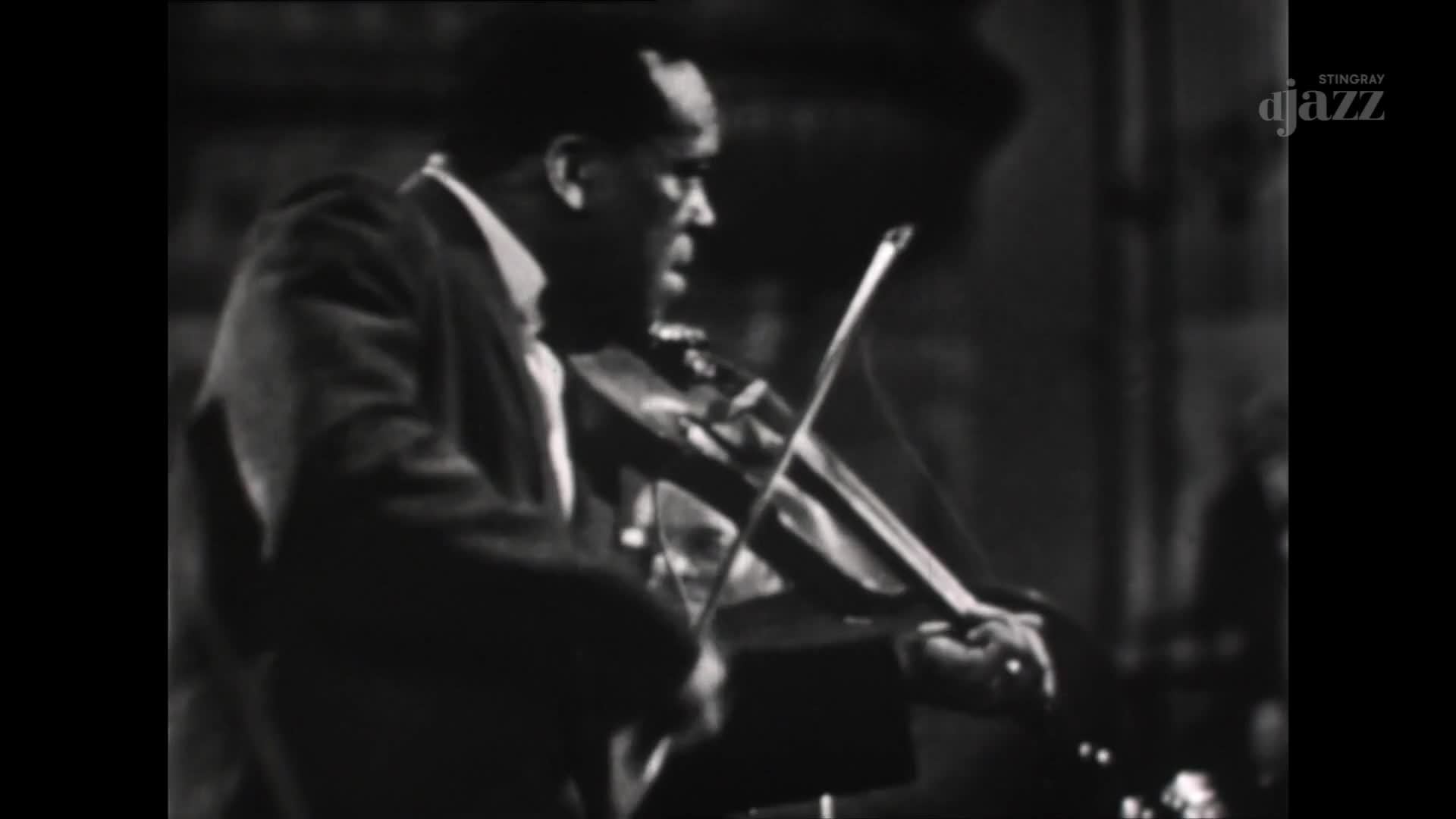 A man in a suit bows his violin, drawing the bow across the strings. The music, broadcast by Stingray DJAZZ in Canada, fills the room.
