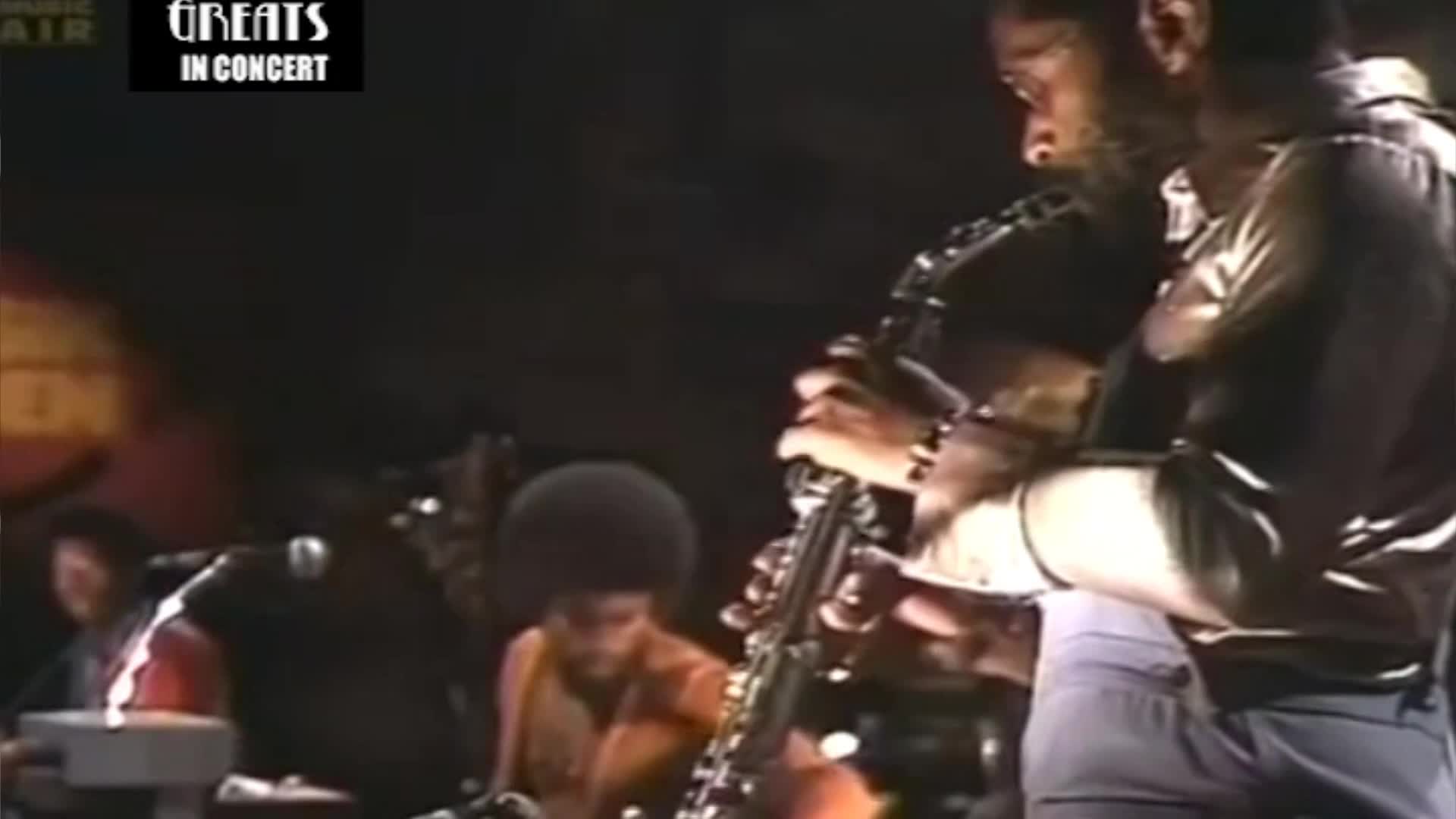 A saxophonist, lit by a spotlight, is blowing into his instrument. The other musicians are in the shadows, but I can make out the drummer and keyboardist.
