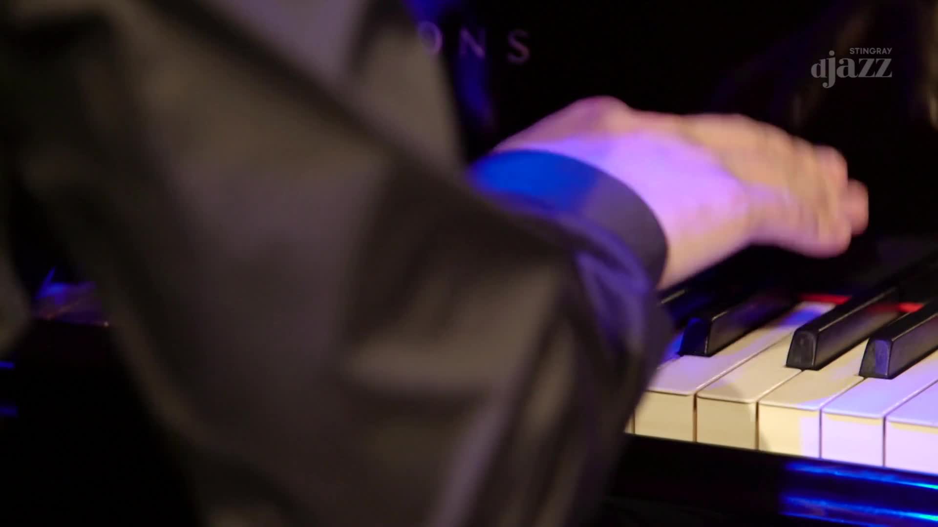 A hand in a dark sleeve hovers over the piano keys, about to strike. The Stingray DJAZZ logo is visible, and the music is about to begin.
