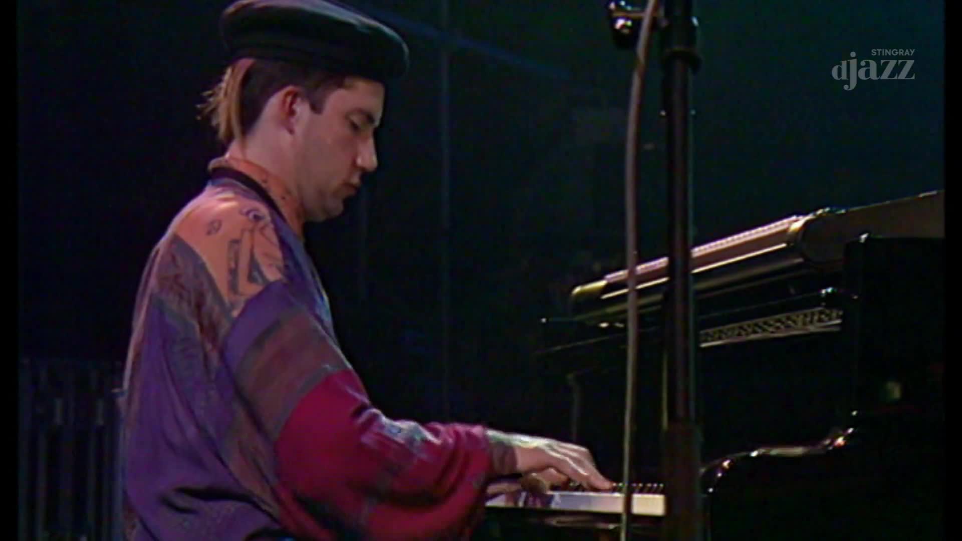 The pianist's fingers dance across the keys, his colorful robe contrasting with the dark piano.  He's focused, bathed in stage light, playing for Stingray DJAZZ in Canada.
