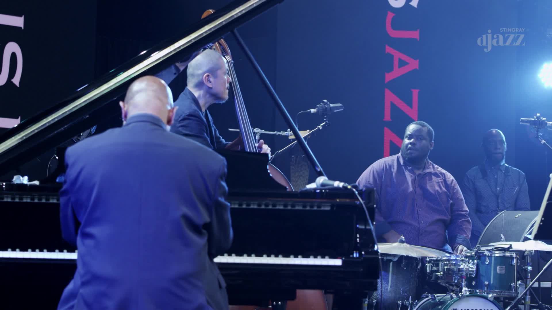 The pianist, in a blue suit, is hunched over the keys, while the bassist leans into his instrument. Across the stage, the drummer sits at his kit, ready to play for Stingray DJAZZ.
The pianist, in a blue suit, is hunched over the keys, while the bassist leans into his instrument. Across the stage, the drummer sits at his kit, ready to play for Stingray DJAZZ.