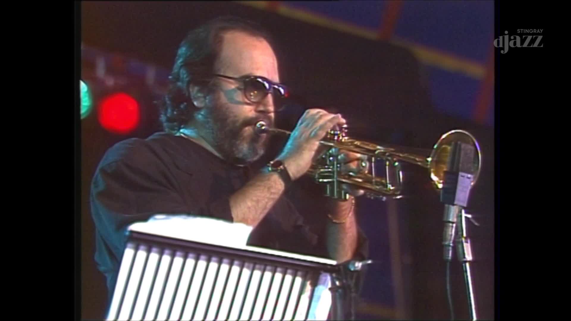 The musician, wearing sunglasses, is blowing into a trumpet, the instrument's brass gleaming under the stage lights. A microphone stands nearby, ready to capture the music for Stingray DJAZZ in Canada.
The musician, wearing sunglasses, is blowing into a trumpet, the instrument's brass gleaming under the stage lights. A microphone stands nearby, ready to capture the music for Stingray DJAZZ in Canada.