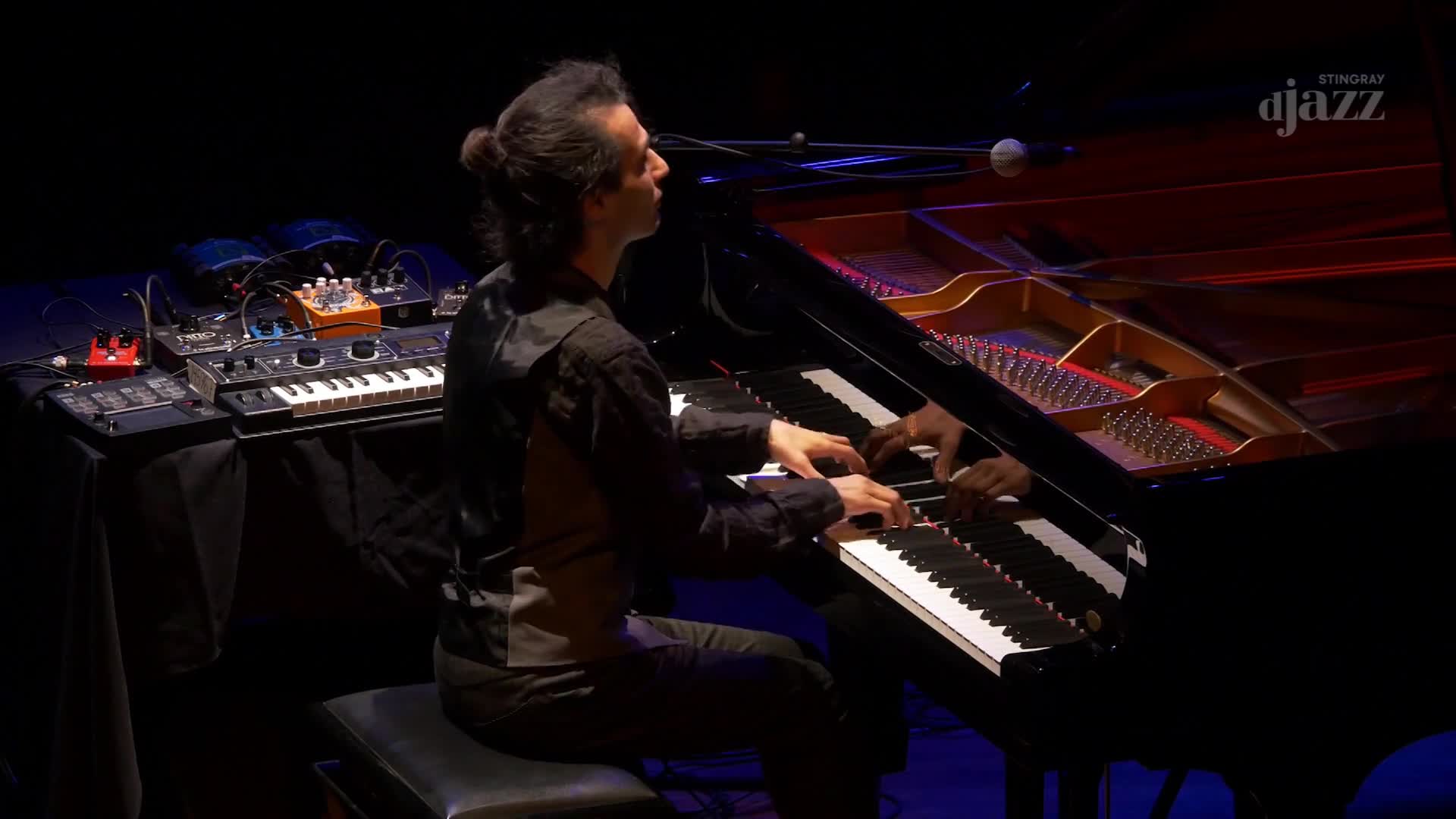 The pianist's fingers dance across the keys of the grand piano, the sound amplified for Stingray DJAZZ. Beside him, a table holds a small synthesizer and other electronic equipment.
The pianist's fingers dance across the keys of the grand piano, the sound amplified for Stingray DJAZZ. Beside him, a table holds a small synthesizer and other electronic equipment.