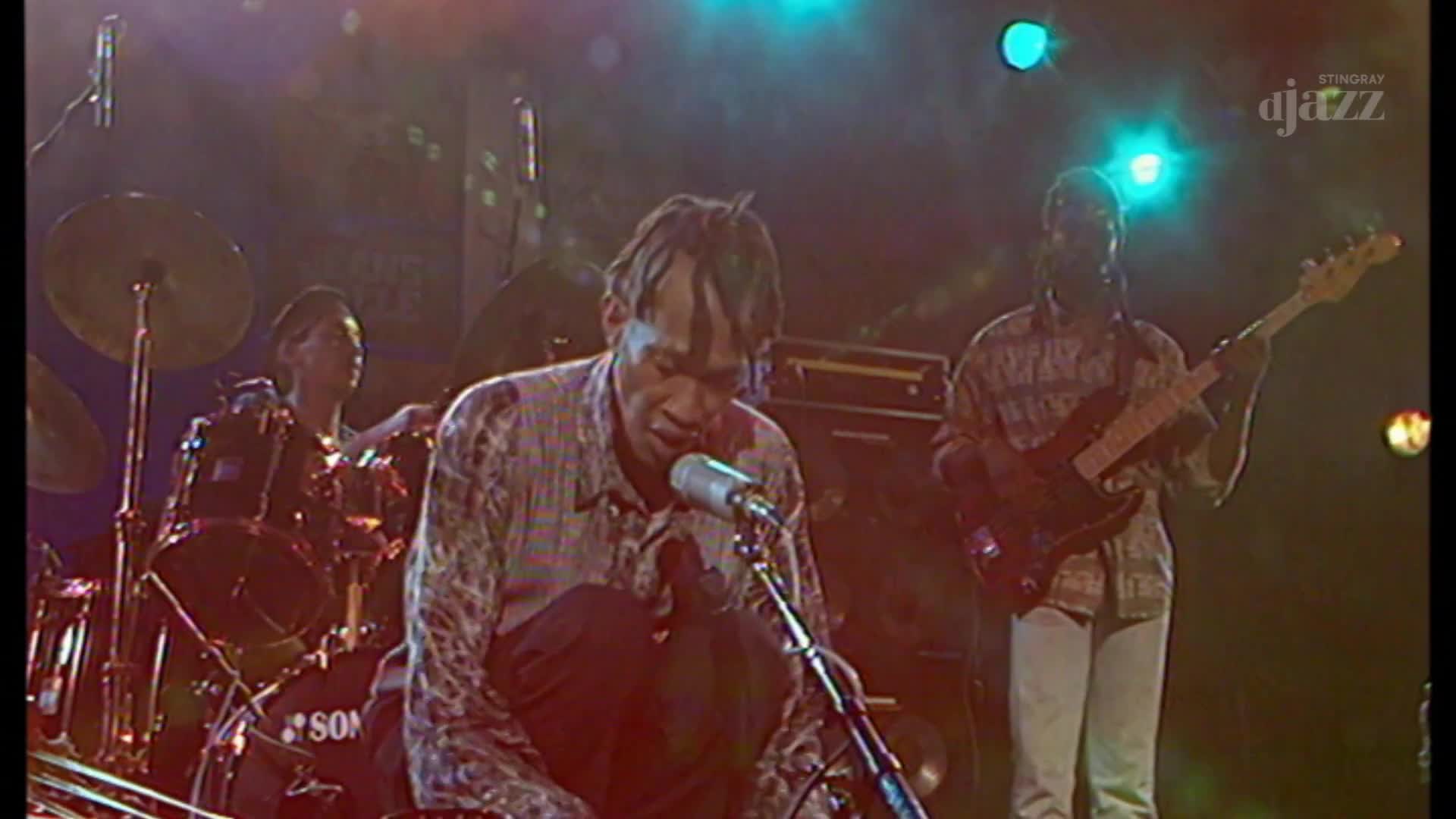 The singer, crouched low, belts into the microphone as the bass player strums next to him. A drummer keeps the beat, and the Stingray DJAZZ logo is visible in the corner.
The singer, crouched low, belts into the microphone as the bass player strums next to him. A drummer keeps the beat, and the Stingray DJAZZ logo is visible in the corner.