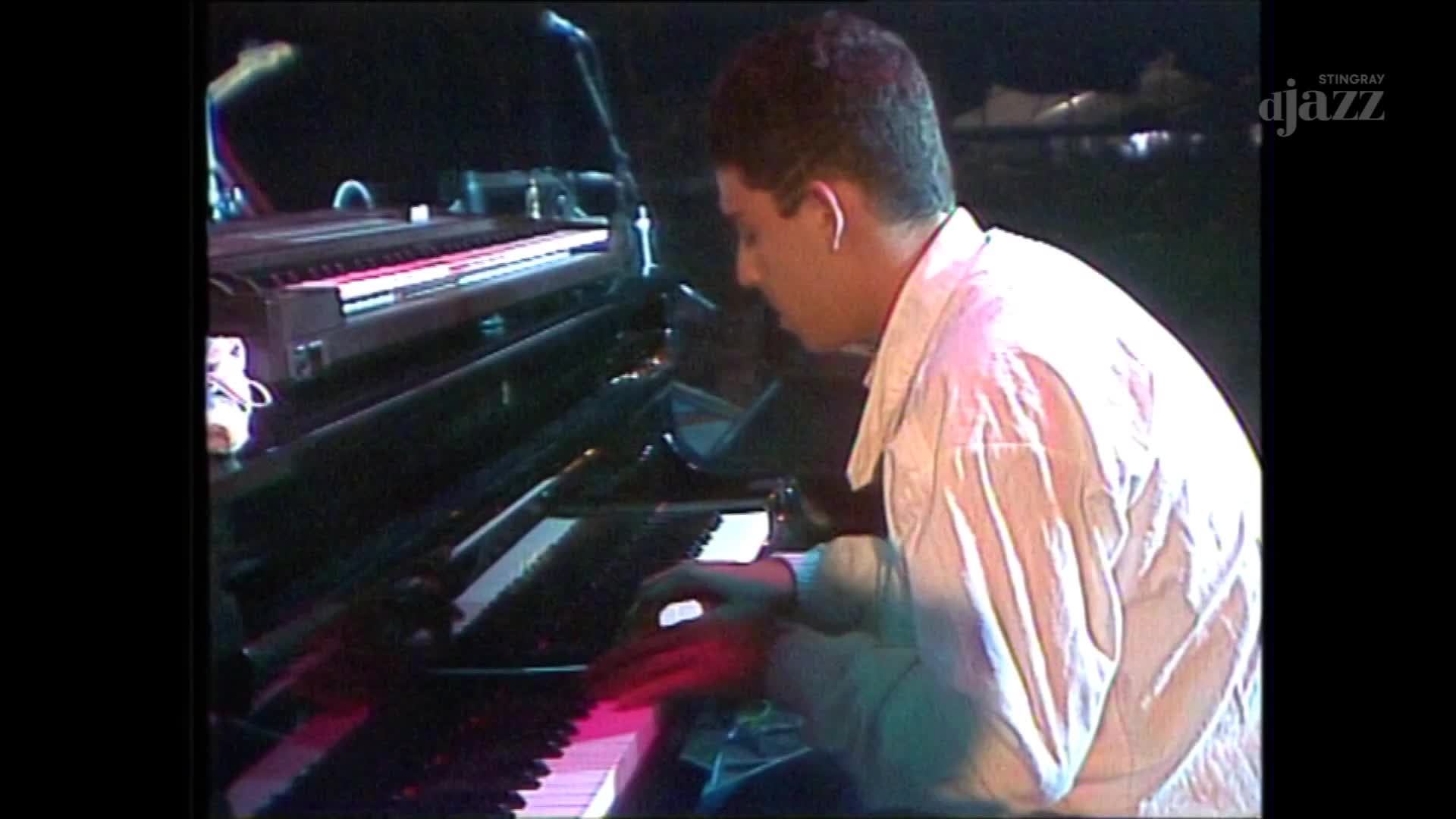 A man in a white shirt plays a grand piano, his hands a blur of motion across the keys. The Stingray DJAZZ logo appears in the corner, hinting at a Canadian broadcast. A man in a white shirt plays a grand piano, his hands a blur of motion across the keys. The Stingray DJAZZ logo appears in the corner, hinting at a Canadian broadcast.