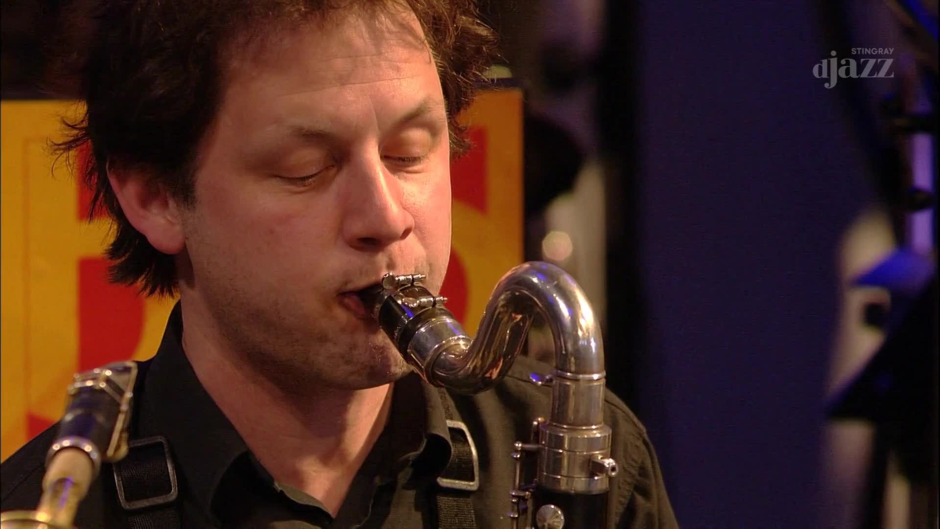 A man in a black shirt plays a clarinet, his eyes closed in concentration. The Stingray DJAZZ logo is visible in the background. A man in a black shirt plays a clarinet, his eyes closed in concentration. The Stingray DJAZZ logo is visible in the background.