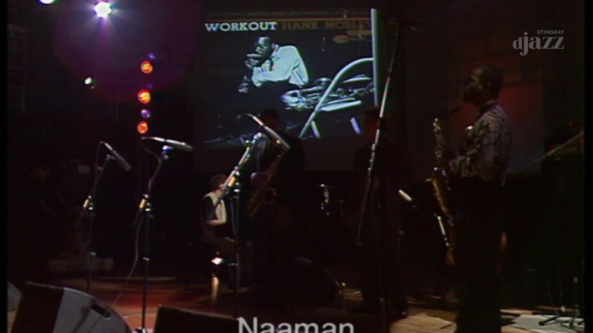 A saxophonist stands on stage, bathed in the glow of a projected image of Hank Mobley. Another musician is seated at a drum kit, partially obscured by shadows. The Stingray djazz logo is visible in the upper right corner. A saxophonist stands on stage, bathed in the glow of a projected image of Hank Mobley. Another musician is seated at a drum kit, partially obscured by shadows. The Stingray djazz logo is visible in the upper right corner.