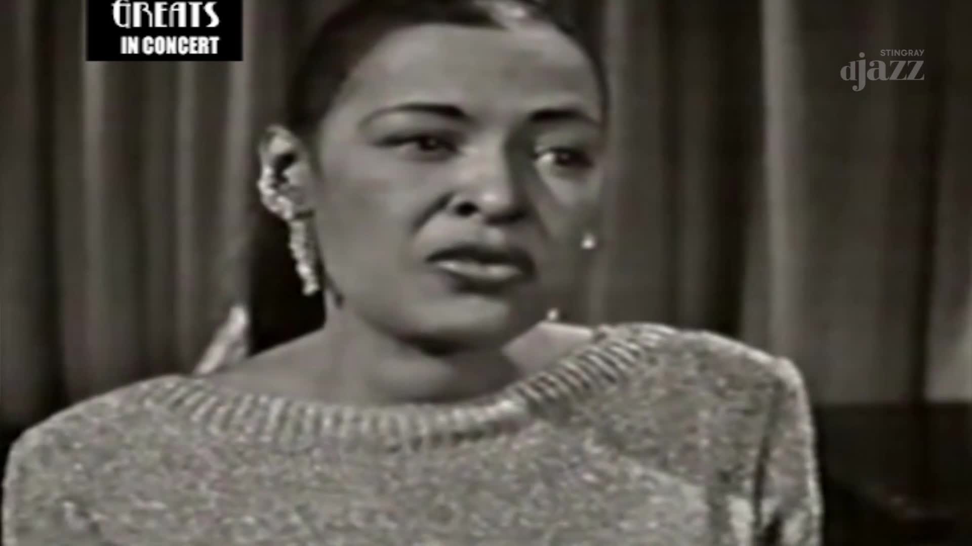 A woman with striking earrings speaks directly to the camera, her expression thoughtful. The "Greats in Concert" logo and Stingray DJAZZ branding appear onscreen. A woman with striking earrings speaks directly to the camera, her expression thoughtful. The "Greats in Concert" logo and Stingray DJAZZ branding appear onscreen.