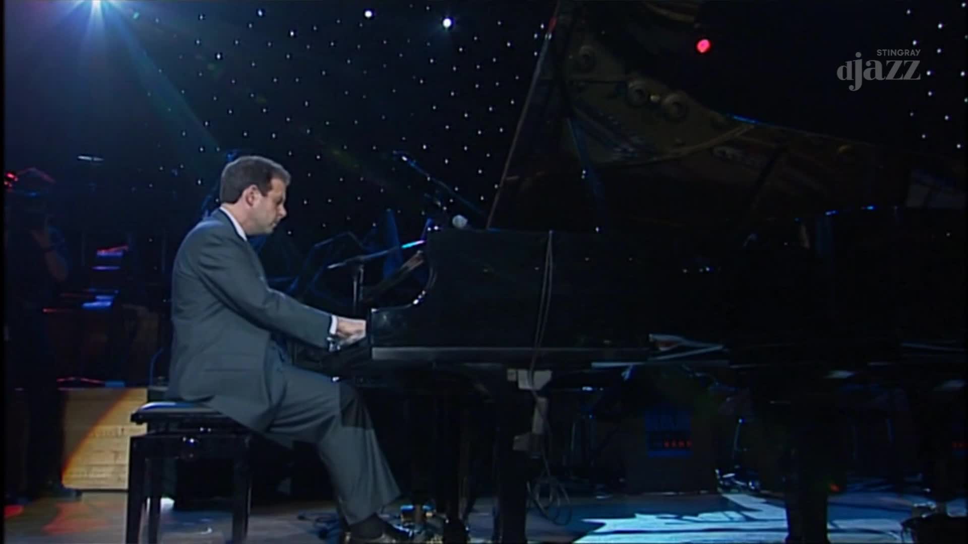A man in a suit plays a grand piano on a stage lit by a starry backdrop. The Stingray DJAZZ logo is visible in the upper right corner.