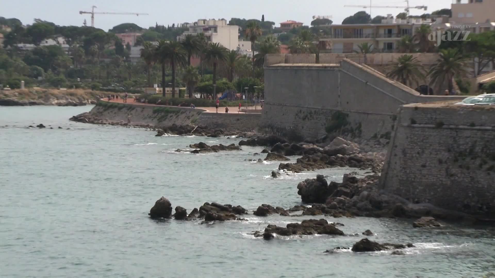 People stroll along the paved path beside the ancient stone fortifications. The calm water laps against the jagged rocks lining the shore. People stroll along the paved path beside the ancient stone fortifications. The calm water laps against the jagged rocks lining the shore.