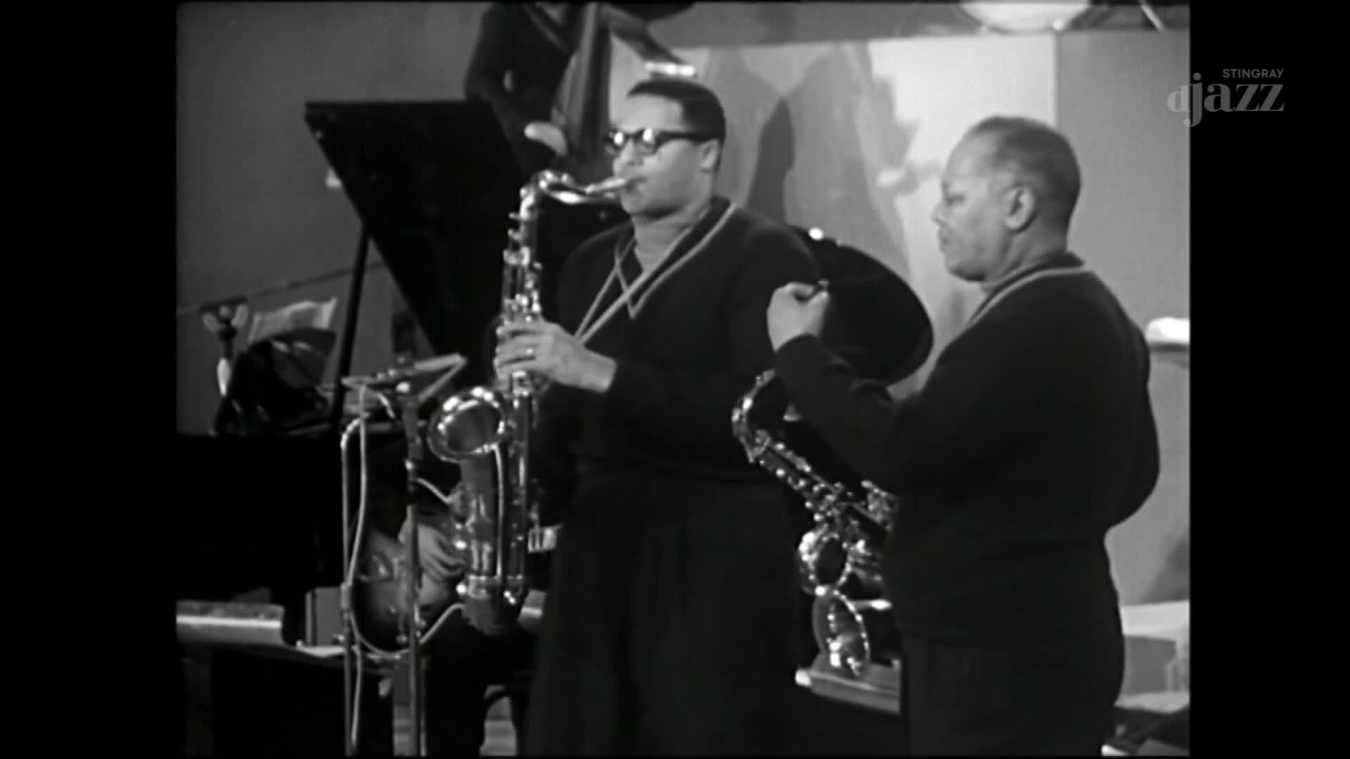 Two saxophonists stand on a stage, one playing a tenor saxophone, the other a smaller alto. The Stingray DJAZZ logo appears in the corner, suggesting this performance is part of a Canadian broadcast. Two saxophonists stand on a stage, one playing a tenor saxophone, the other a smaller alto. The Stingray DJAZZ logo appears in the corner, suggesting this performance is part of a Canadian broadcast.