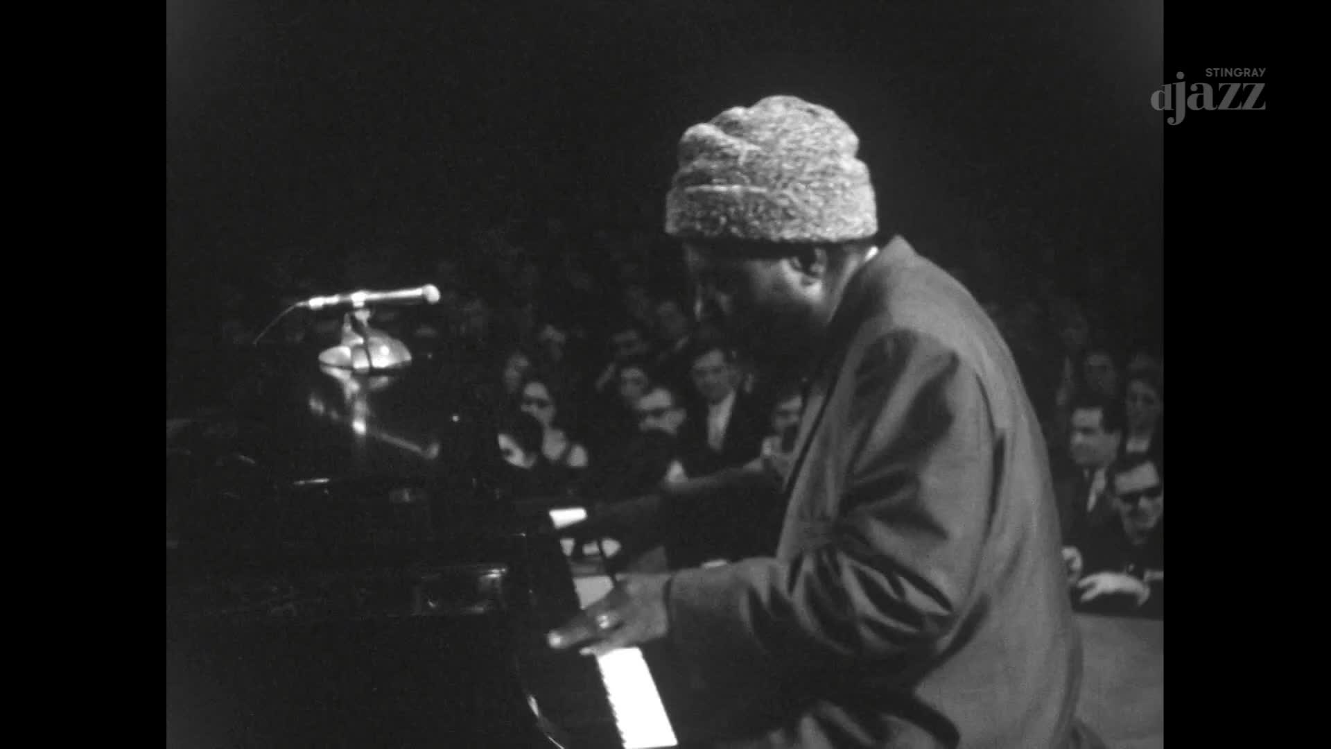 A pianist in a fuzzy hat plays a grand piano on a stage in front of a seated audience. The Stingray DJAZZ logo appears in the corner, hinting at a broadcast from Canada.