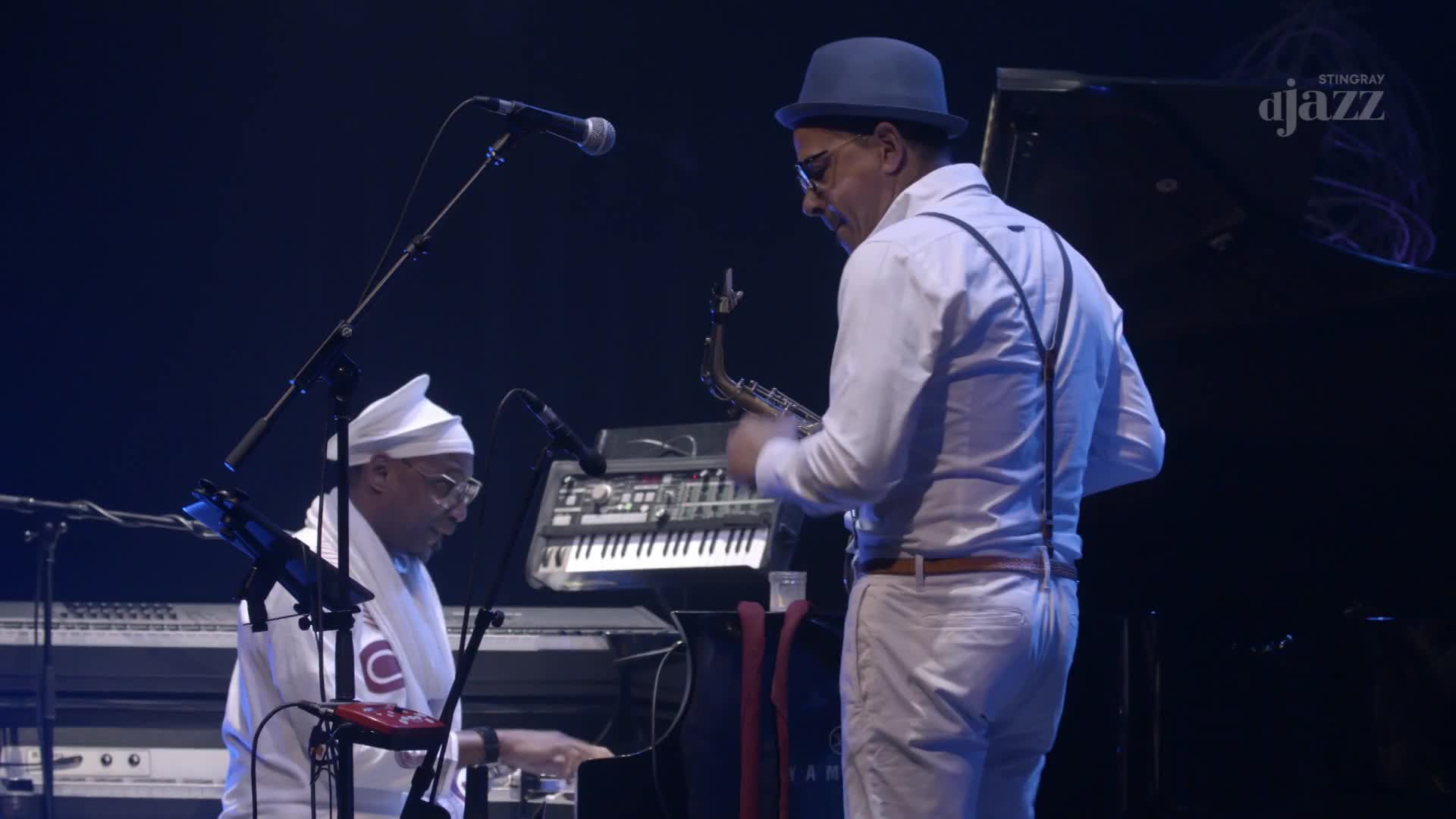 A man in a white cap and robe plays a keyboard, while a man in a blue hat and suspenders holds a saxophone. The Stingray dJazz logo is visible in the background.