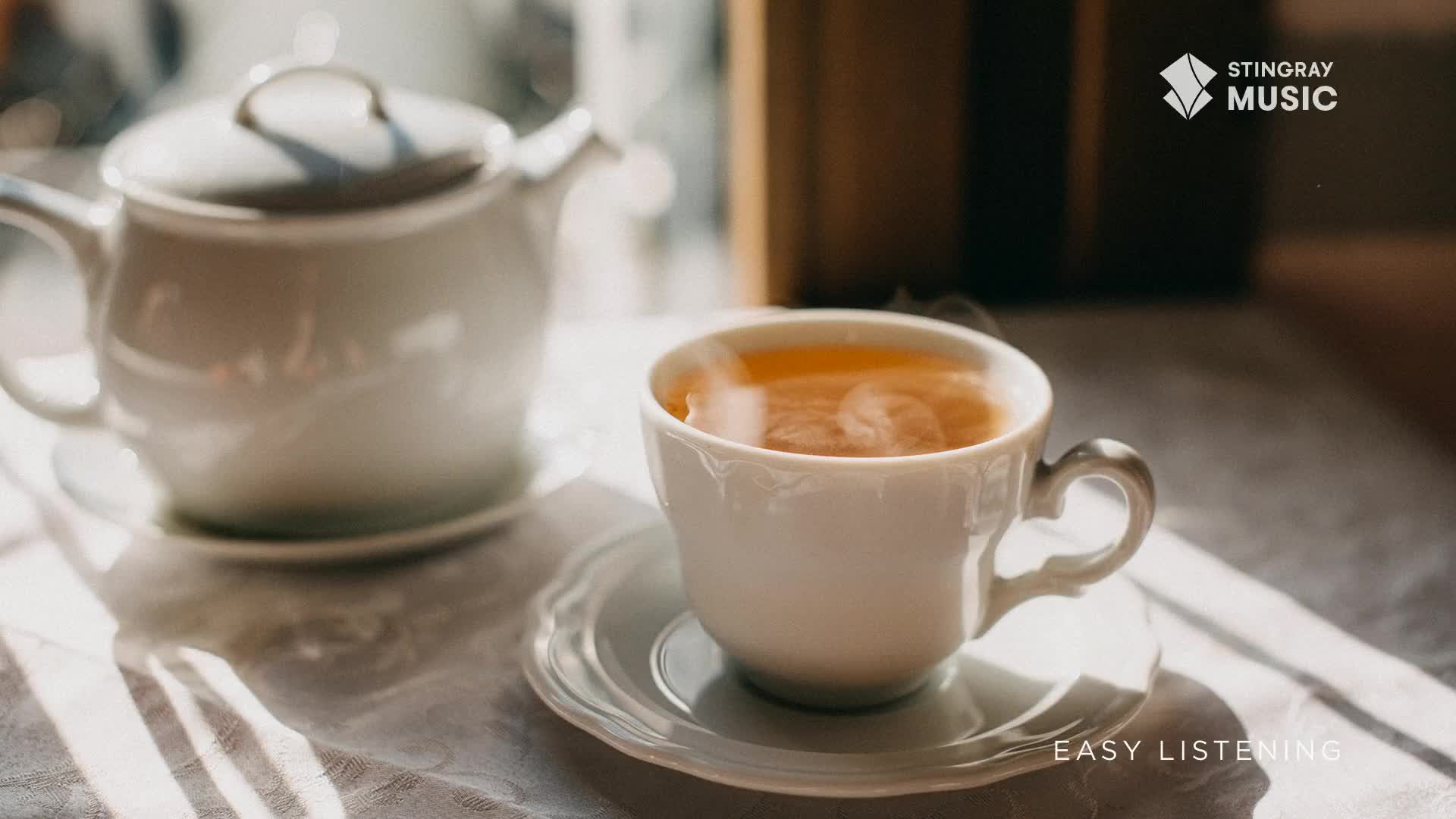 A white teacup sits on a saucer, filled with steaming amber liquid. Sunlight streams in, catching the wisps of vapor rising from the tea.

