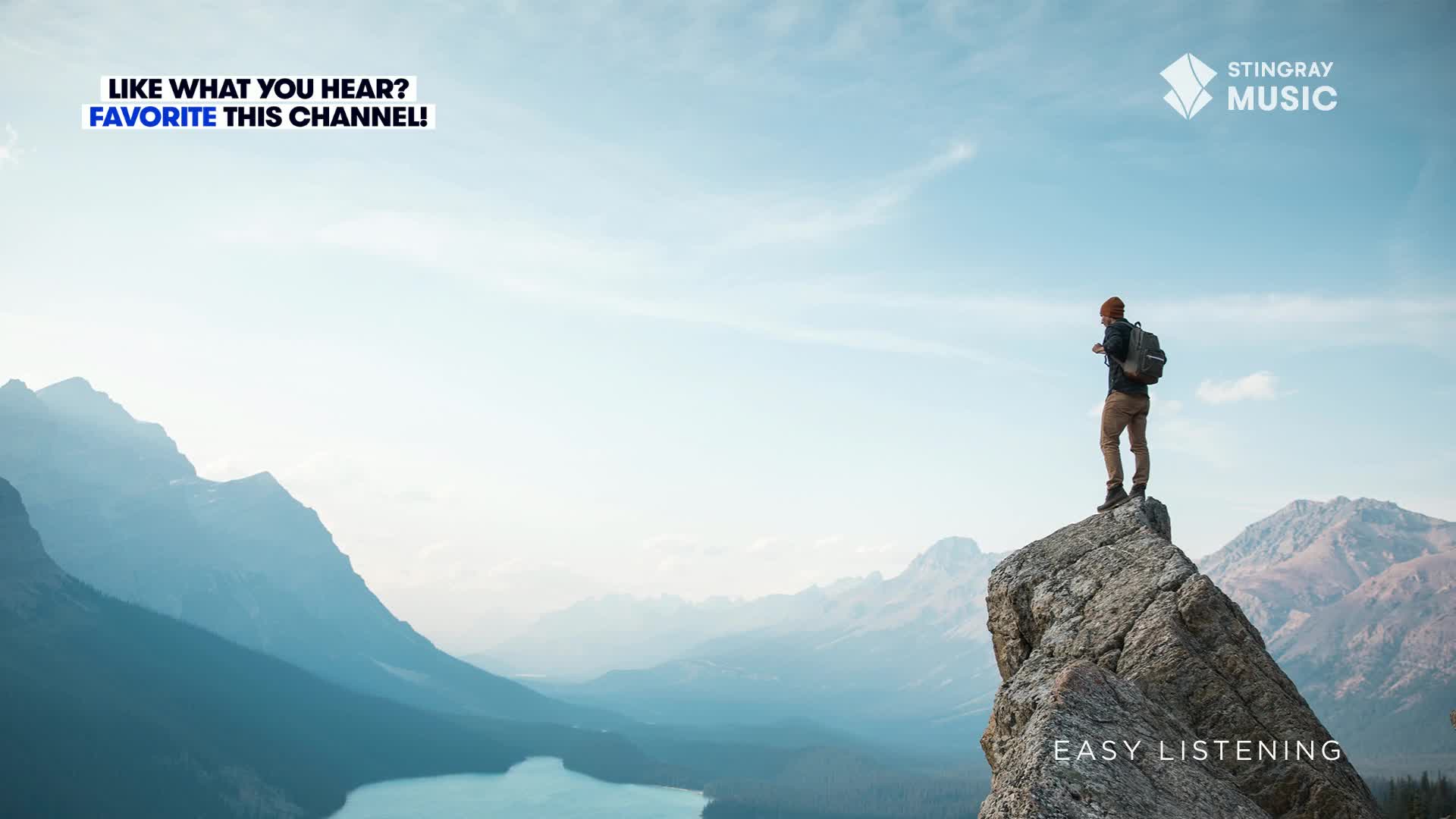 A person stands on a rocky peak, gazing out at the vast mountain range. The Stingray Easy Listening logo is in the corner, and the scene feels like Canada.
