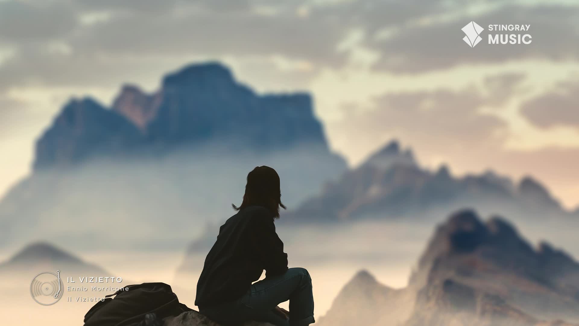 A person sits on a rocky outcrop, gazing at the misty Canadian mountains. The Stingray Music logo sits in the corner, the perfect soundtrack for this quiet moment.
