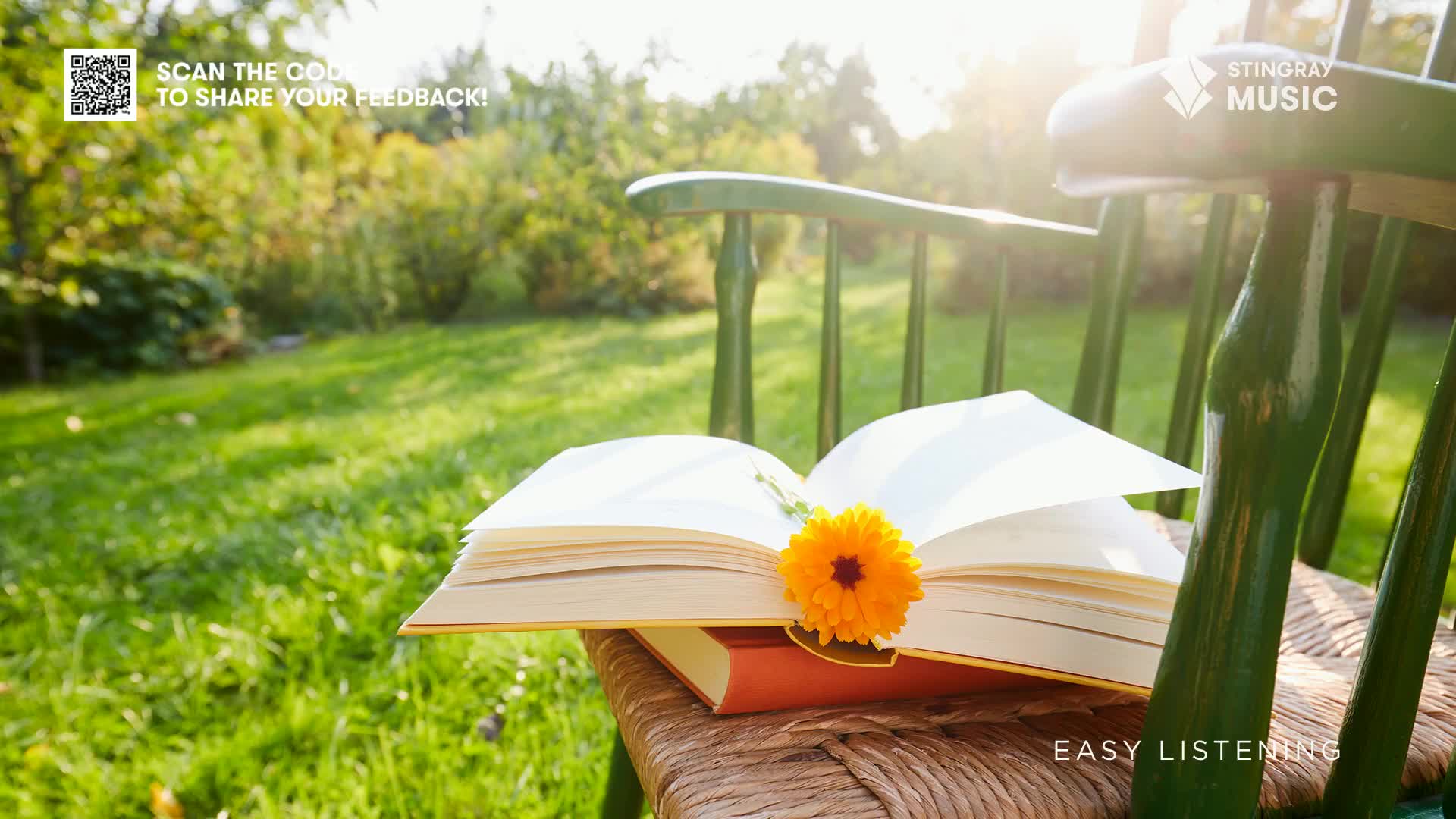 Sunlight streams through the trees, illuminating an open book resting on a wicker chair. A single orange flower sits nestled among the pages, inviting a moment of calm, perhaps while listening to Stingray Easy Listening, in Canada.
