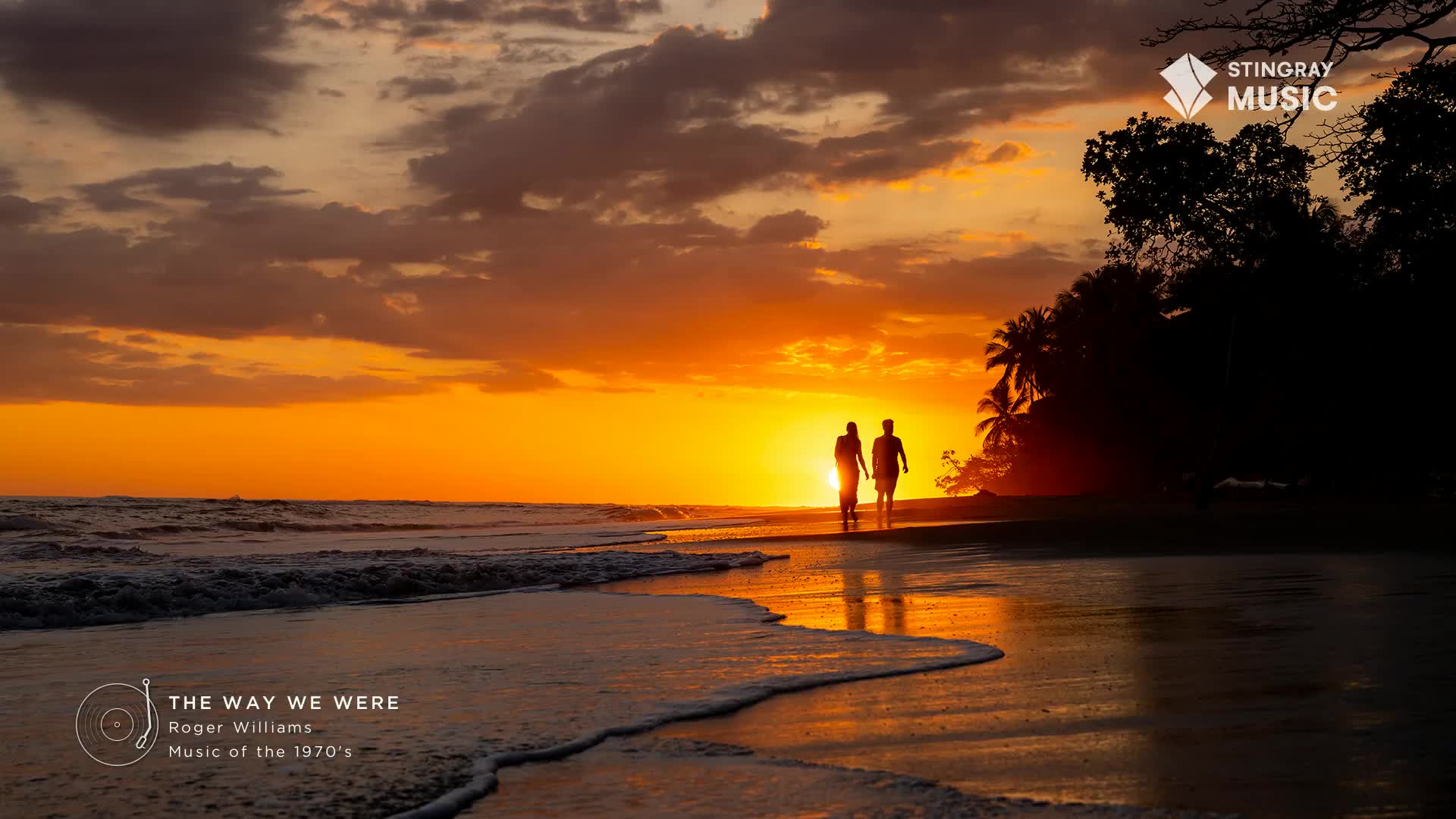 The sun is setting, painting the sky in fiery hues as a couple strolls along the water's edge. The waves gently lap the shore, reflecting the warm glow, a scene that could easily accompany the Stingray Easy Listening station from Canada.
