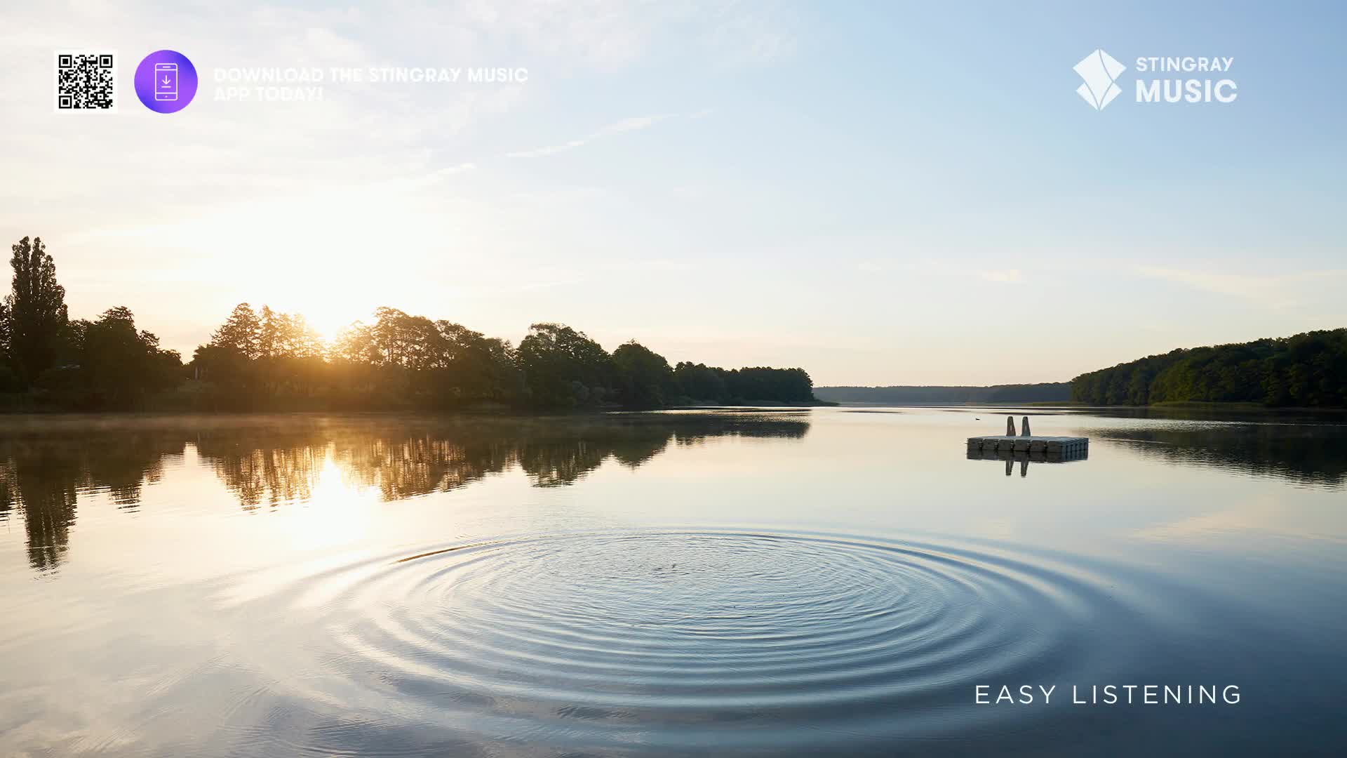 The sun is rising over the trees, its light reflecting on the still water. A small splash has created concentric circles spreading across the lake, a perfect image for the easy listening vibes.
