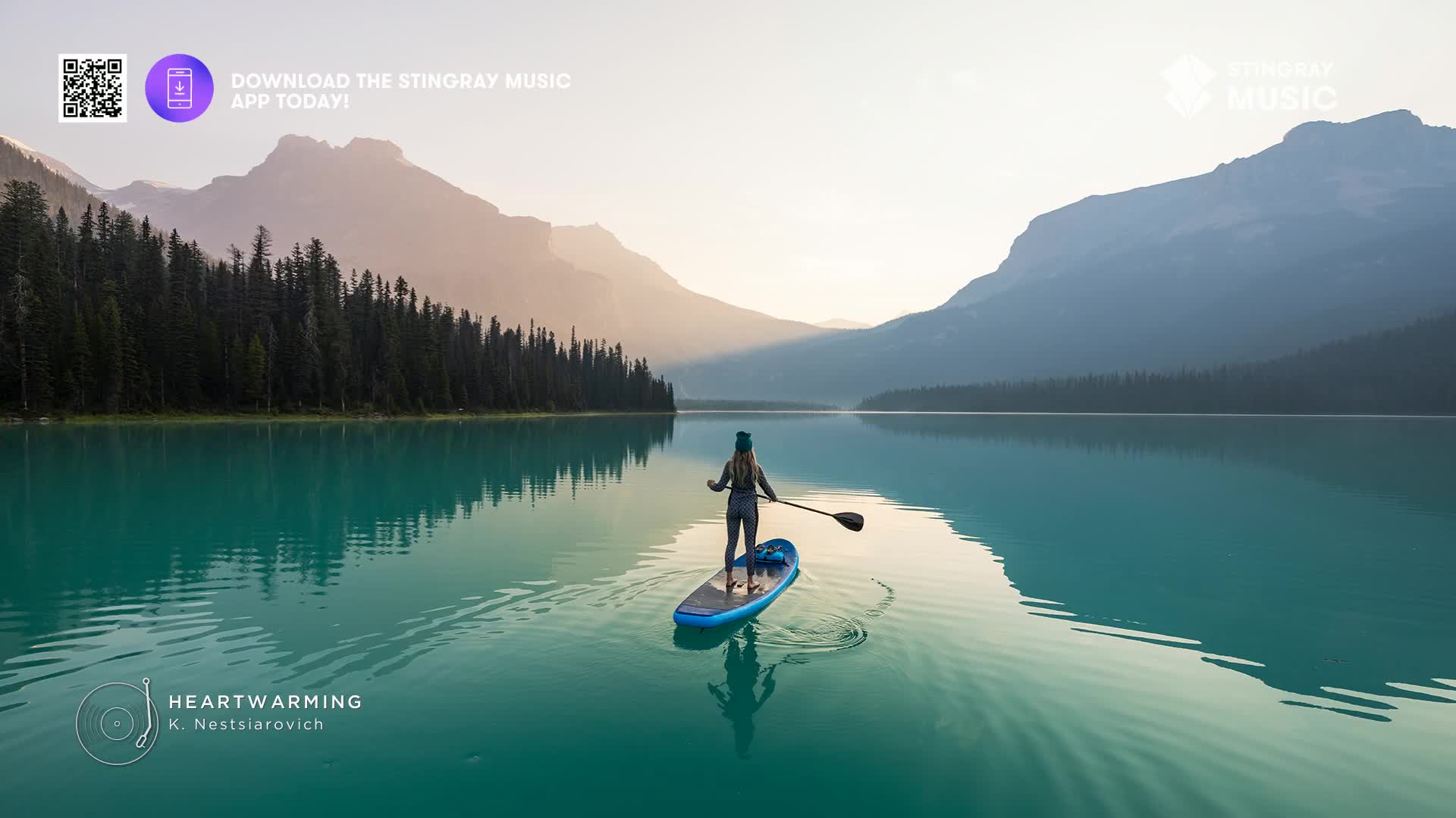 A person on a paddleboard glides across the still, turquoise water, the mountains of Canada rising in the distance. The scene feels peaceful, like the kind of music you might hear on Stingray Easy Listening.
