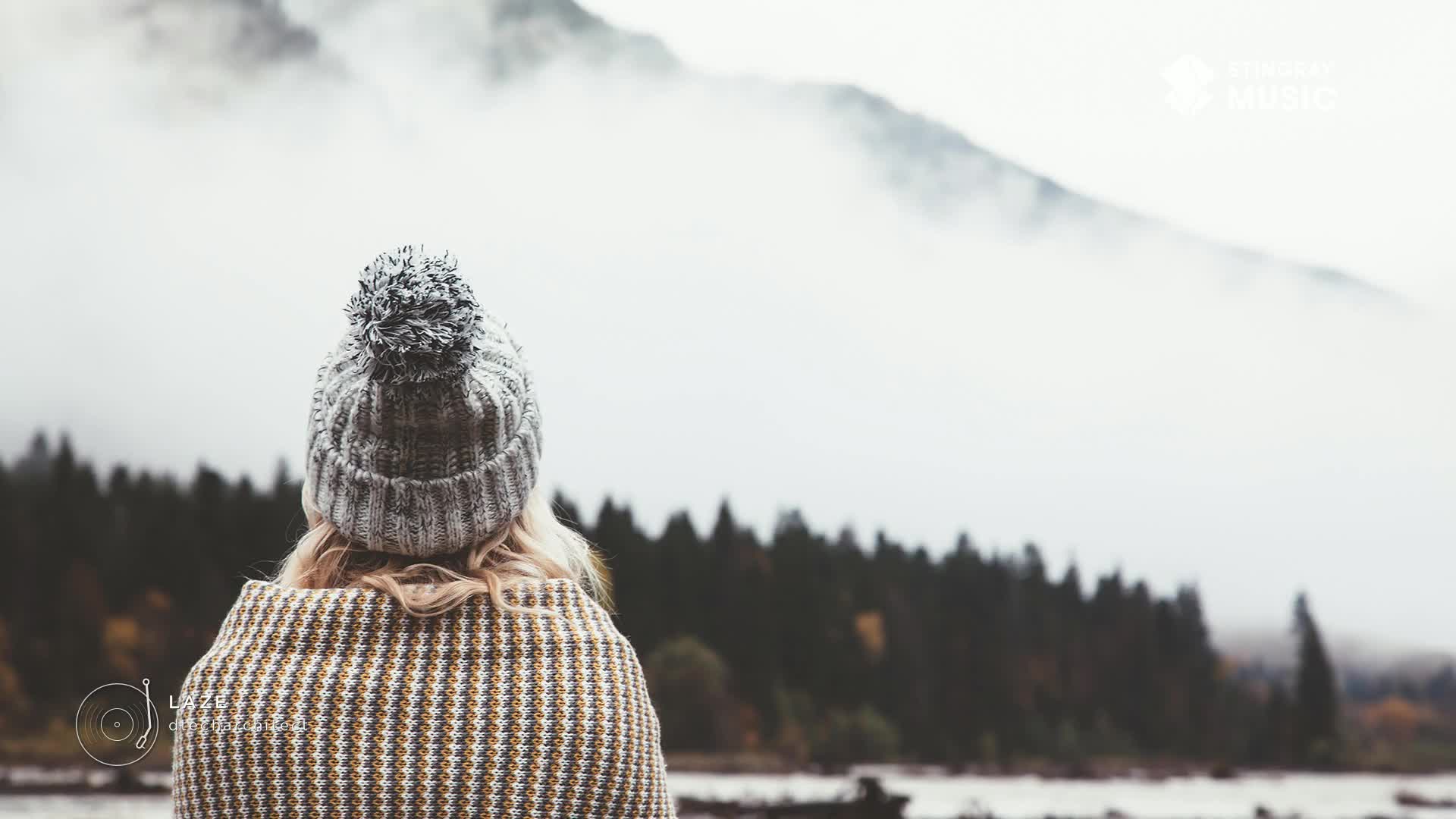 A person in a knitted hat and patterned wrap faces a misty mountain range. The air feels crisp, the scene perfect for some Stingray Easy Listening from Canada.

