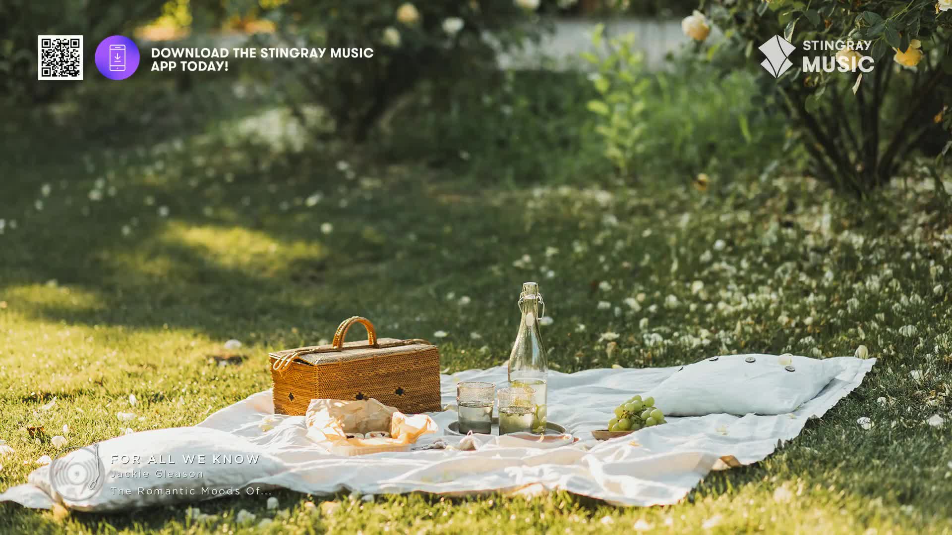A picnic blanket sits on the grass, with a basket, bottle, and grapes arranged on top. The scene feels calm, like the kind of music you might hear on Stingray Easy Listening in Canada.
