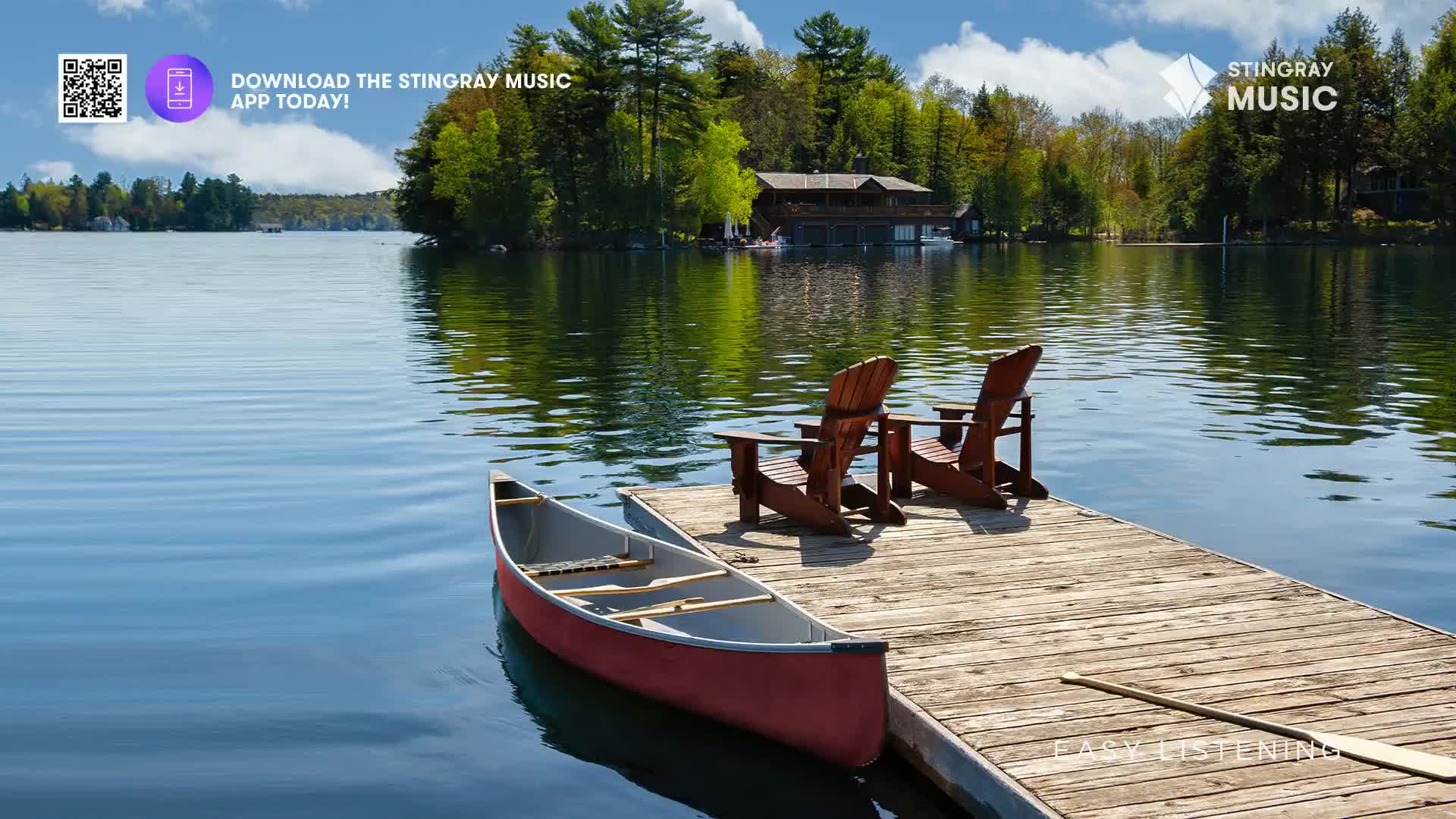 A red canoe rests on a wooden dock, ready for a leisurely paddle on the calm Canadian lake. Two wooden Adirondack chairs face each other, inviting a moment of peaceful contemplation, perhaps while listening to Stingray Easy Listening.
