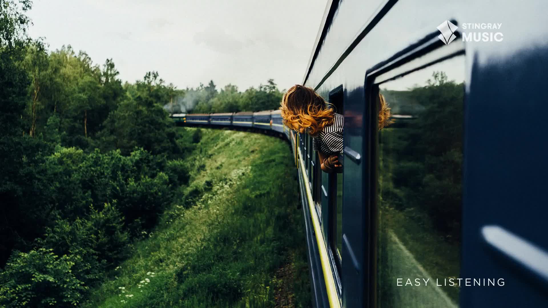A train, its blue side reflecting the passing trees, curves along the track. A person leans out the window, their hair blowing in the wind, as the train heads through the Canadian countryside.
A train, its blue side reflecting the passing trees, curves along the track. A person leans out the window, their hair blowing in the wind, as the train heads through the Canadian countryside.