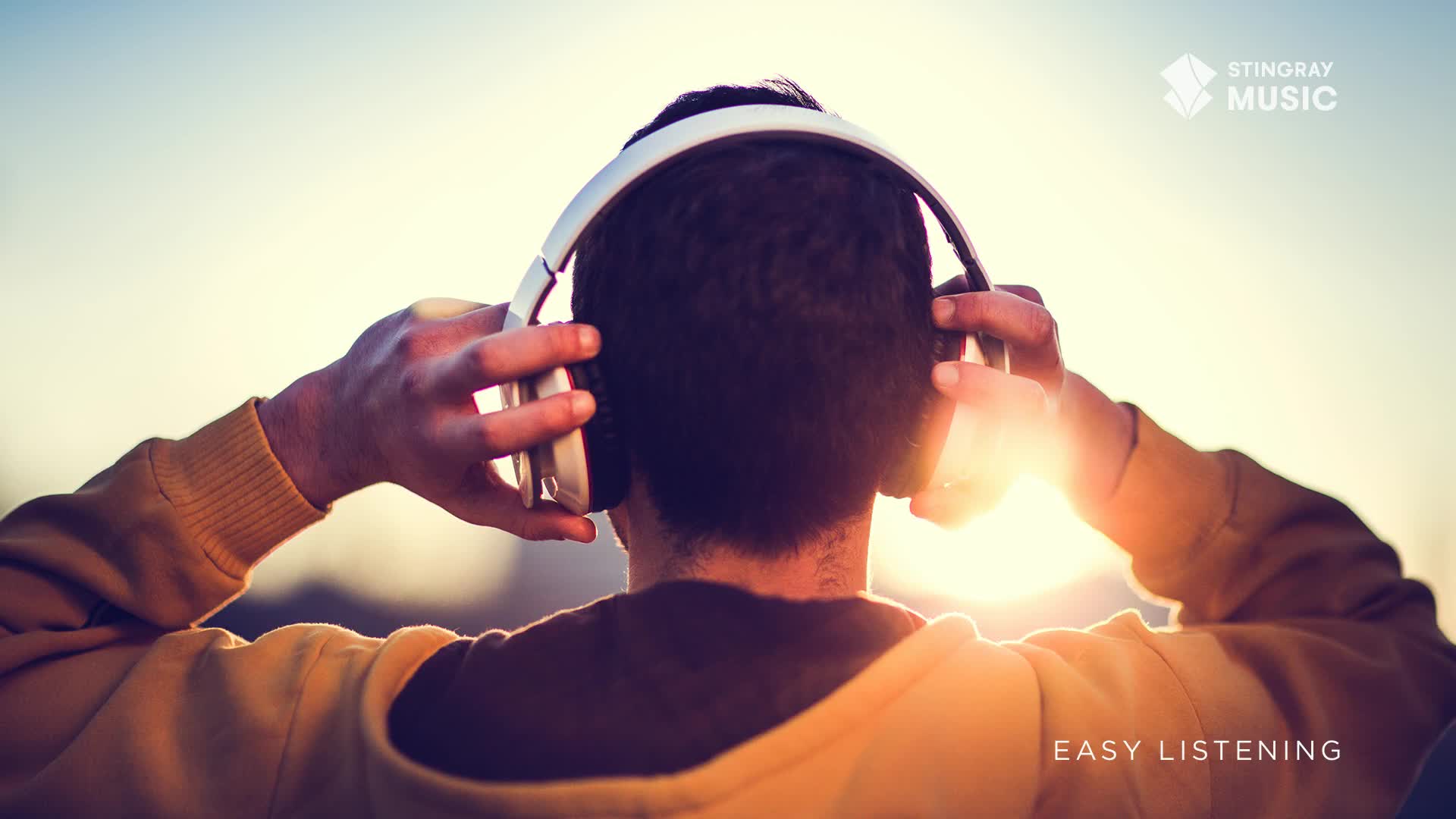 A person is wearing headphones, their hands resting on the earcups. The sun shines brightly behind them, as if they're enjoying some Stingray Easy Listening.
