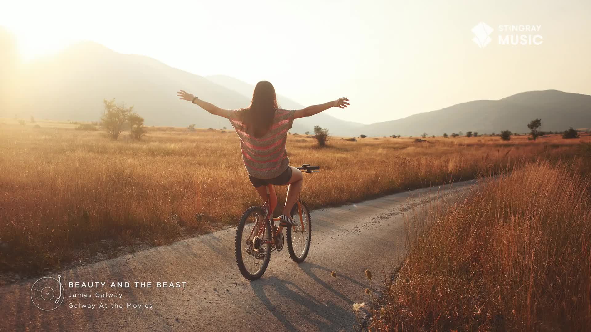 A young woman, arms outstretched, rides a bicycle down a sun-drenched path. The landscape, bathed in golden light, feels like a scene from a Stingray Easy Listening commercial, somewhere in Canada.
