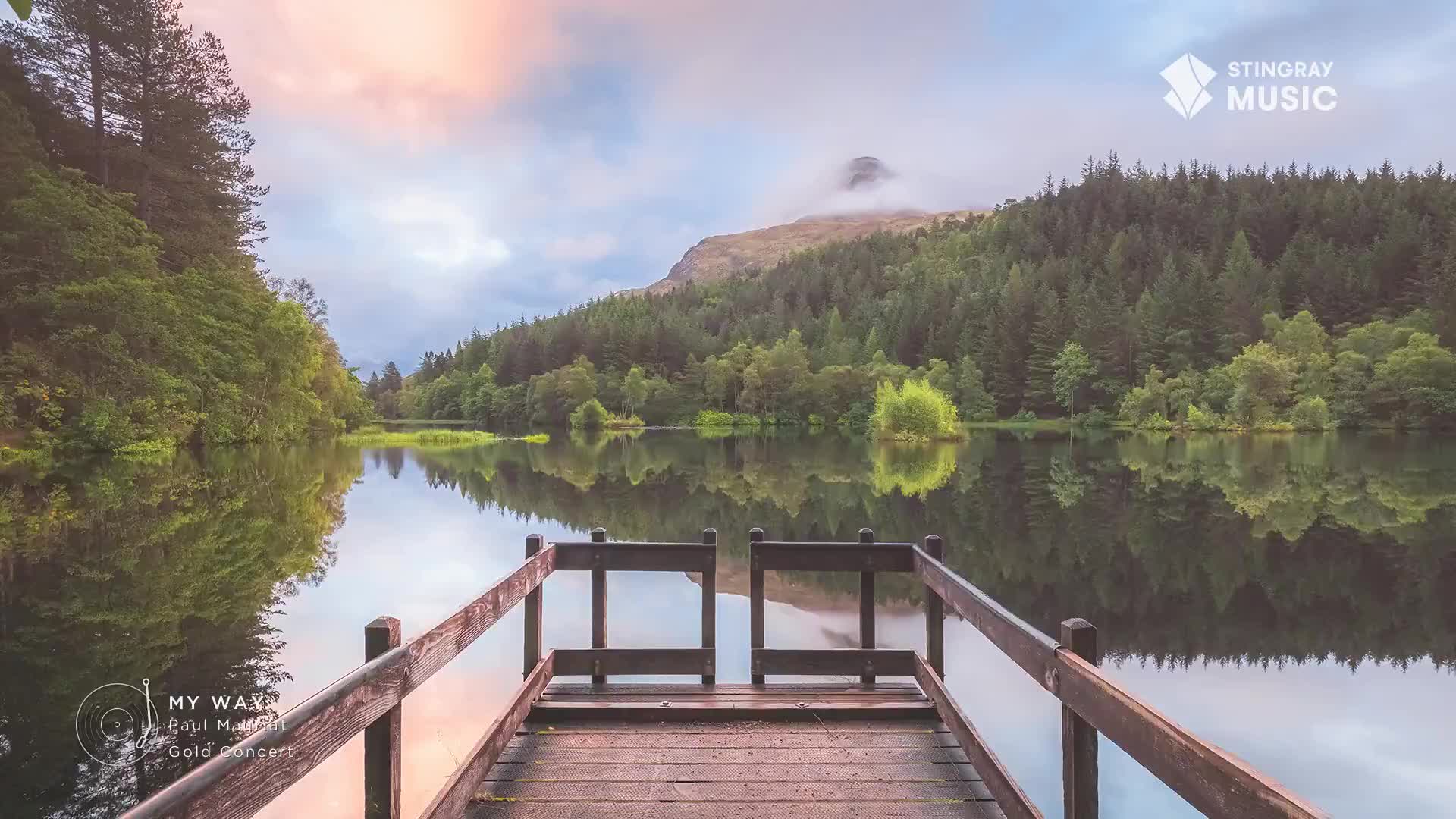 A wooden dock extends over still water, mirroring the trees and a distant mountain. The sky is a blend of soft pinks and blues, a perfect backdrop for the Canadian landscape, likely playing on Stingray Easy Listening.
A wooden dock extends over still water, mirroring the trees and a distant mountain. The sky is a blend of soft pinks and blues, a perfect backdrop for the Canadian landscape, likely playing on Stingray Easy Listening.