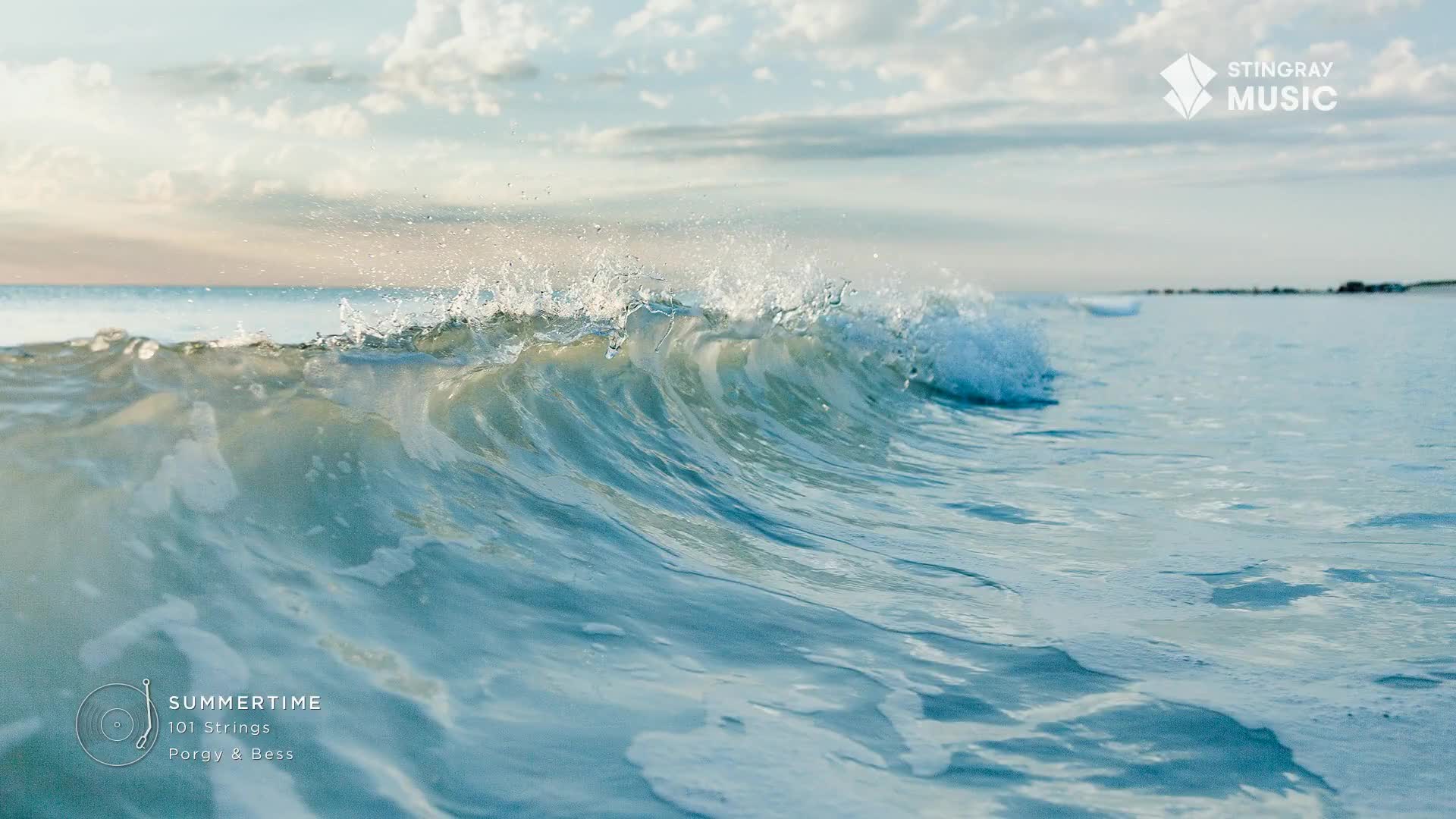 A wave crests and breaks, sending spray into the air. The water is a clear, cool blue, reflecting the soft light of a Canadian summer sky.