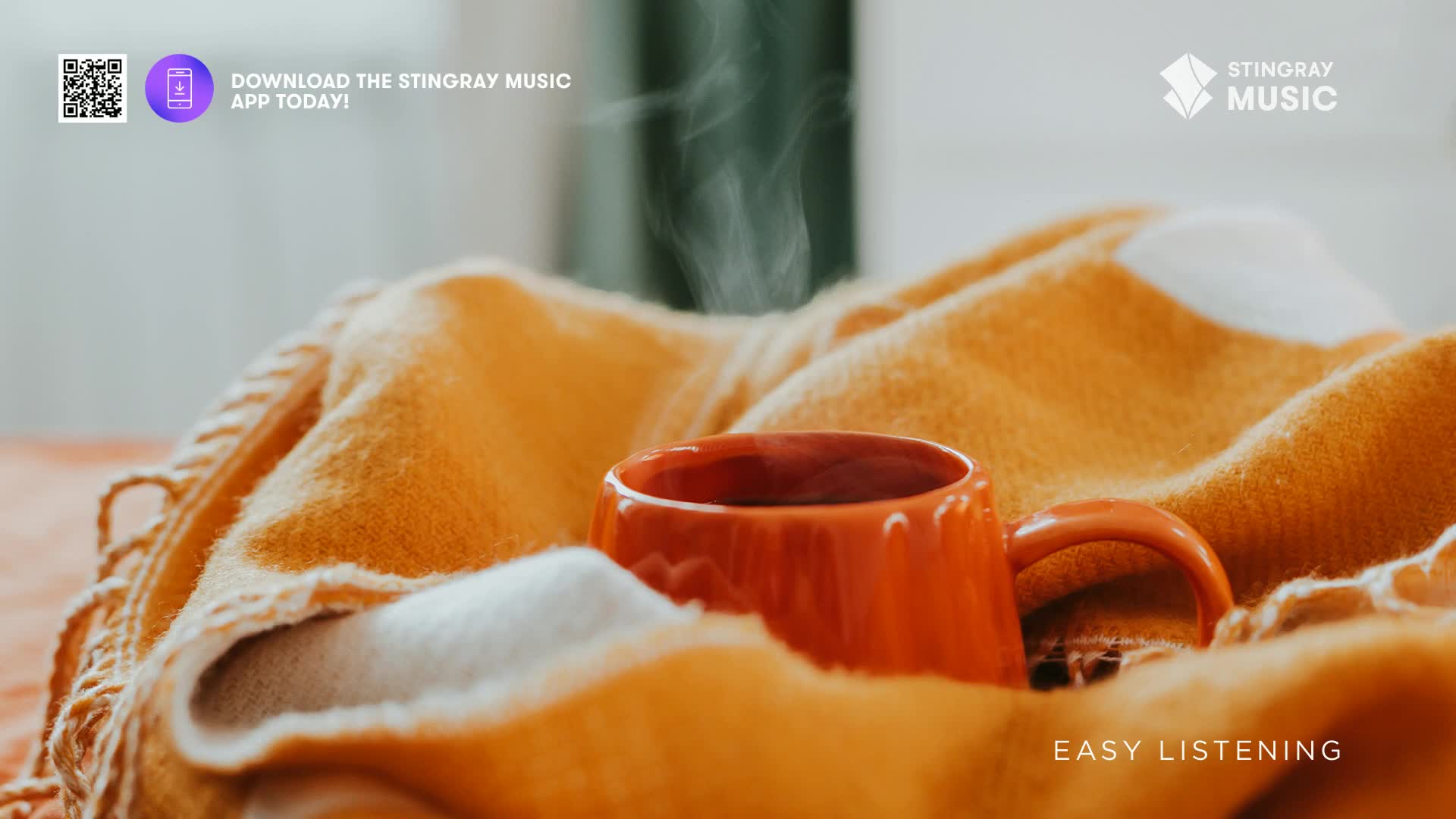Steam rises from a bright orange mug nestled in a cozy, textured blanket. The soft folds of the fabric create a warm embrace around the cup.