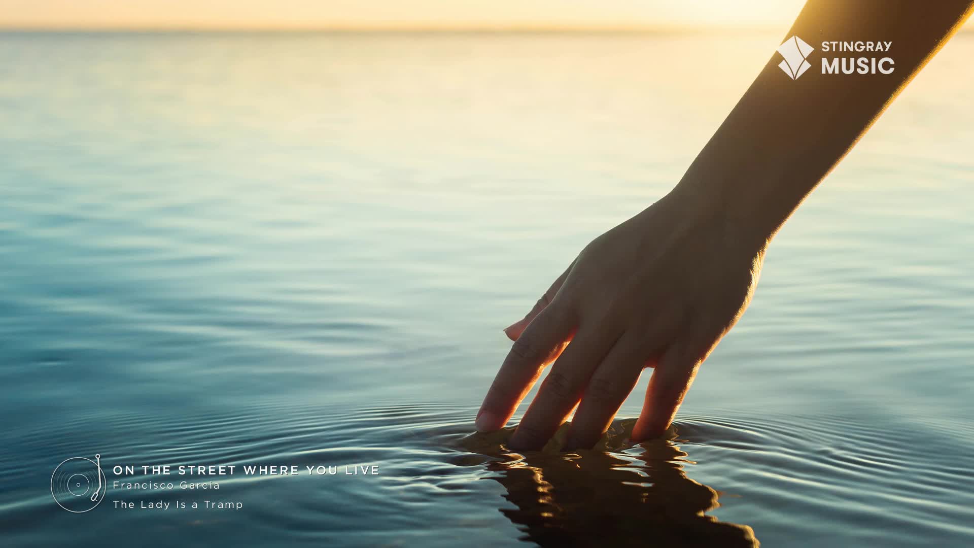 Fingertips skim the surface of the calm water, creating gentle ripples. The late afternoon sun casts a warm glow over the scene, a perfect moment for Stingray Easy Listening.