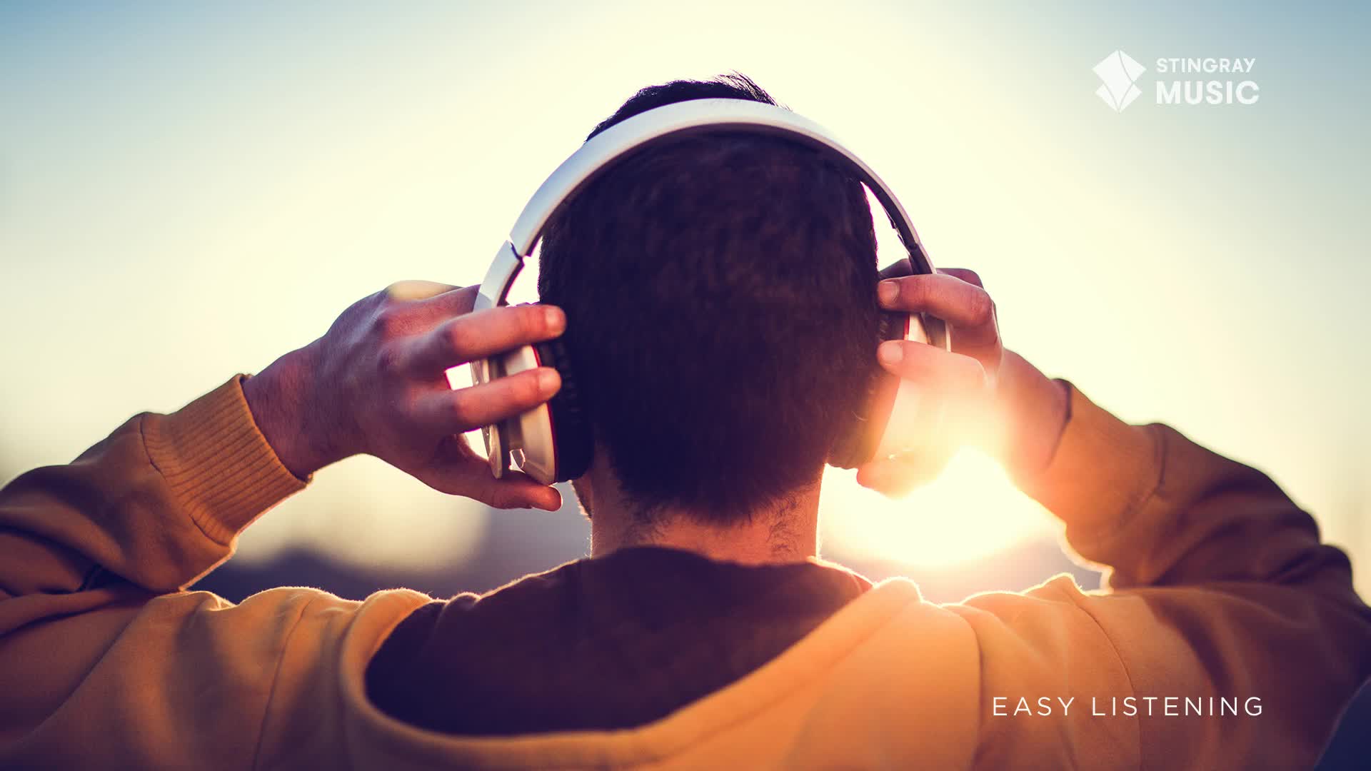 The sun is setting behind a person wearing white headphones, their hands adjusting them. The warm glow of the sun highlights the back of their head and shoulders as they seem to be enjoying some Stingray Easy Listening. The sun is setting behind a person wearing white headphones, their hands adjusting them. The warm glow of the sun highlights the back of their head and shoulders as they seem to be enjoying some Stingray Easy Listening.
