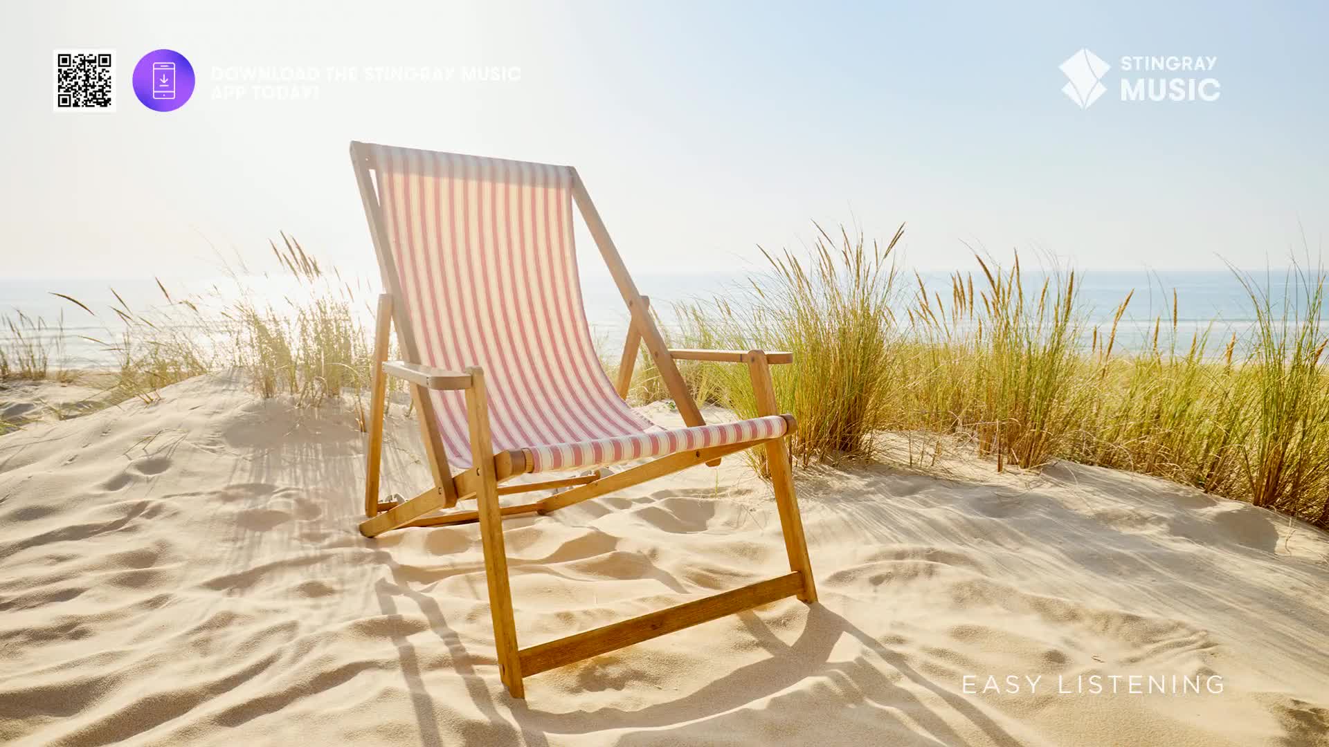 A gentle breeze rustles the tall grasses on the sand dunes, just like the kind of sound you'd hear on a Stingray Easy Listening channel. The sun shines brightly on an empty beach chair, waiting for someone to settle in and enjoy the view.